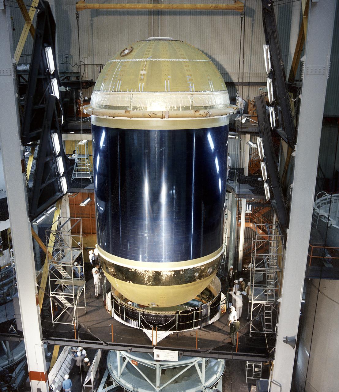 Assembling activities of the Skylab cluster are shown in this photograph. The Orbital Workshop (OWS) was lowered for joining to aft skirt and placed over the thrust structure inside the assembly tower. The OWS provided living and working quarters for the Skylab crew and the thruster provided short-term attitude control of the Skylab. The Marshall Space Flight Center had responsibilities for the design and development of the Skylab hardware, and management of experiments. 