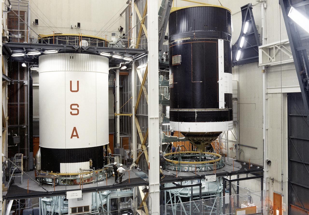 This photograph shows activities during assembly of the Skylab cluster at the Vehicle Assembly/Checkout building. The Saturn V S-IVB stage is shown at left, and right is the Orbital Workshop (OWS) being readied for mating to the thruster. The S-IVB stage was modified to house the OWS, which provided living and working quarters for the Skylab crews. The Marshall Space Flight Center had responsibilities for the design and development of the Skylab hardware, and management of experiments. 