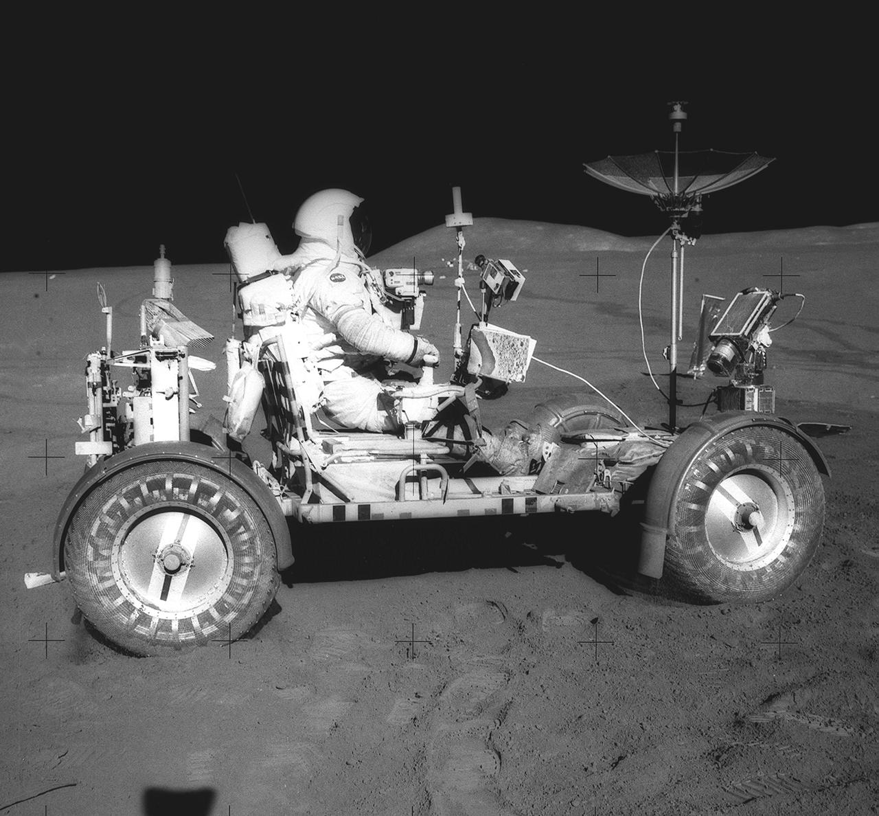 This photograph was taken during the Apollo 15 mission on the lunar surface. Astronaut David R. Scott waits in the Lunar Roving Vehicle (LRV) for astronaut James Irwin for the return trip to the Lunar Module, Falcon, with rocks and soil collected near the Hadley-Apernine landing site. The Apollo 15 was the first mission to use the LRV. Powered by battery, the lightweight electric car greatly increased the range of mobility and productivity on the scientific traverses for astronauts. It weighed 462 pounds (77 pounds on the Moon) and could carry two suited astronauts, their gear and cameras, and several hundred pounds of bagged samples. The LRV's mobility was quite high. It could climb and descend slopes of about 25 degrees. The LRV was designed and developed by the Marshall Space Flight Center and built by the Boeing Company. 