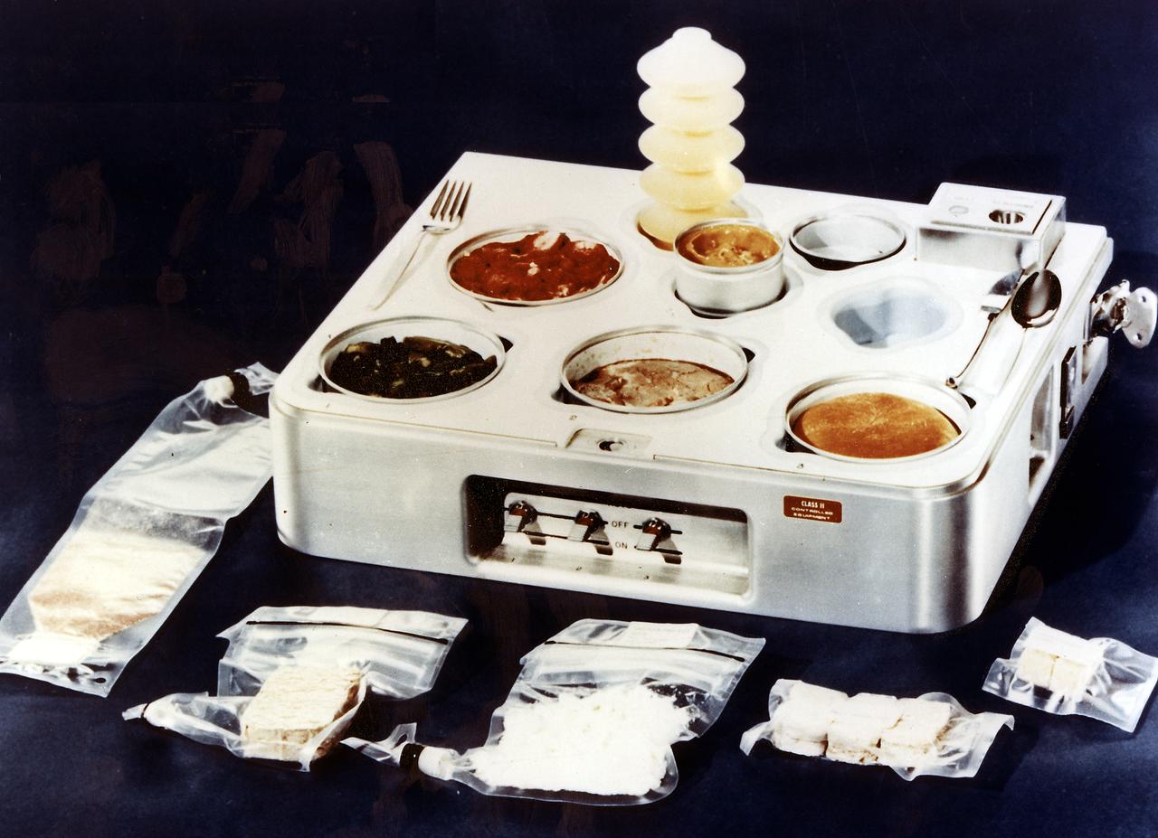 Shown here is the Skylab food heating and serving tray with food, drink, and utensils. The tray contained heating elements for preparing the individual food packets. The food on Skylab was a great improvement over that on earlier spaceflights. It was no longer necessary to squeeze liquified food from plastic tubes. Skylab's kitchen in the Orbital Workshop wardroom was so equipped that each crewman could select his own menu and prepare it to his own taste. The Marshall Space Flight Center had program management responsibility for the development of Skylab hardware and experiments. 