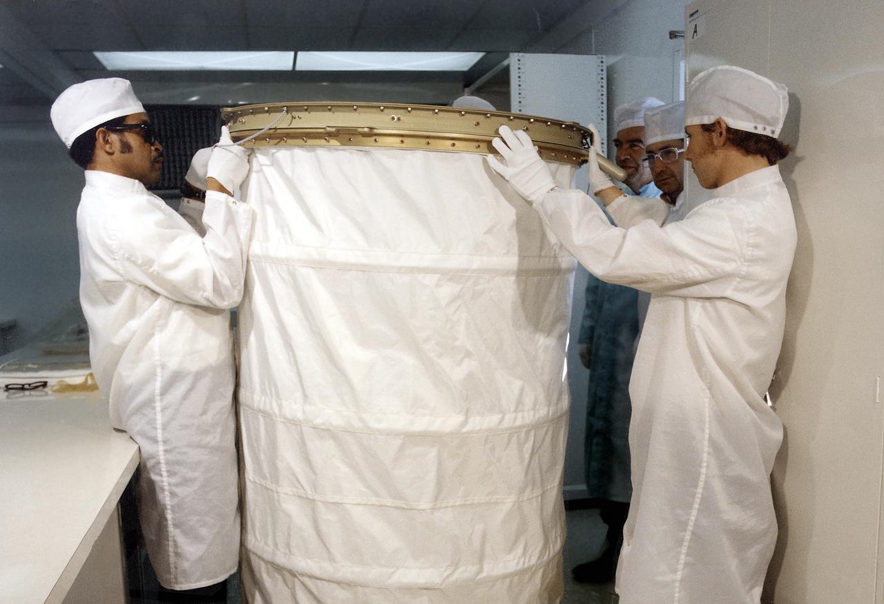 In this photograph, the Orbital Workshop shower compartment was unfolded by technicians for inspection. The shower compartment was a cylindrical cloth enclosure that was folded flat when not in use. The bottom ring of the shower was fastened to the floor and contained foot restraints. The upper ring contained the shower head and hose. To use the shower, the astronaut filled a pressurized portable bottle with heated water and attached the bottle to the ceiling. A flexible hose cornected the water bottle to a handheld shower head. The astronaut pulled the cylindrical shower wall up into position and bathed, using liquid soap. Both soap and water were carefully rationed, having been premeasured for economical use.
