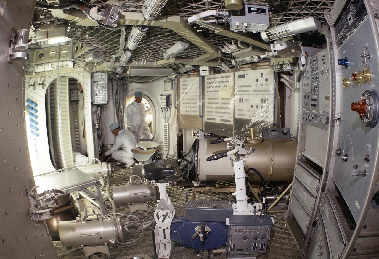 This is a wide-angle view of the Orbital Workshop lower level experiment area. In center foreground is the ergometer bicycle. In center background is a litter chair for the Human Vestibular Function experiment (Skylab Experiment M131) and in right background is the Lower Body Negative Pressure System experiment (Skylab Experiment M092). The ergometer bicycle was used for metabolic activity experiments and exercise. The purpose of the Human Vestibular (irner ear) Function experiment was to examine the effect of weightlessness on man's sensitivity and susceptibility to motion rotation, and his perception of orientation. The Lower Body Negative Pressure experiment investigated the relationship between the zero gravity environment and cardiovascular deconditioning. A characteristic of cardiovascular deconditoning is the partial failure of the blood vessels resulting in the excessive pooling of the blood in the legs when a person assumes an erect posture in a gravity field. The Marshall Space Flight Center had the program management responsibility for the development of Skylab hardware and experiments. 