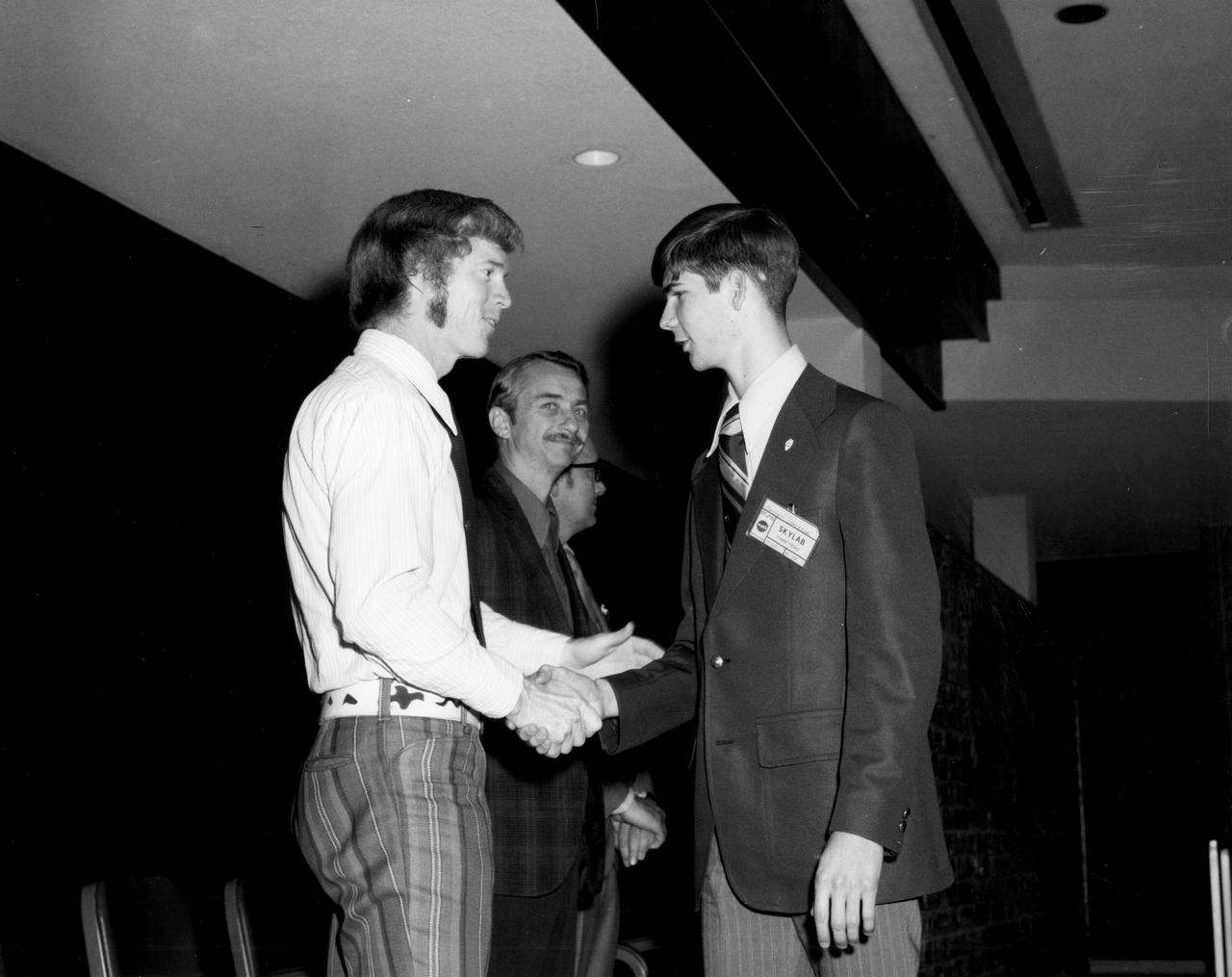 Rockford, Illinois high school student, Vincent Converse (right), is greeted by astronauts Russell L. Schweickart and Owen K. Garriott during a tour of the Marshall Space Flight Center (MSFC).  Converse was among 25 winners of a contest in which some 3,500 high school students proposed experiments for the following year’s Skylab mission. His experiment, “Zero Gravity Mass Measurement” used a simple leaf spring with the mass to be weighed attached to the end.  An electronic package oscillated the spring at a specific rate and the results were recorded electronically. The nationwide scientific competition was sponsored by the National Science Teachers Association and the National Aeronautics and Space Administration (NASA). The winning students, along with their parents and sponsor teachers, visited MSFC where they met with scientists and engineers, participated in design reviews for their experiments, and toured MSFC facilities. Of the 25 students, 6 did not see their experiments conducted on Skylab because the experiments were not compatible with Skylab hardware and timelines. Of the 19 remaining, 11 experiments required the manufacture of additional equipme