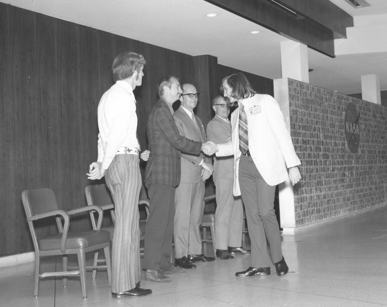 Springfield, Massachusetts high school student, Gregory A. Merkel, is greeted by (left to right): Astronauts Russell L. Schweickart, and Owen K. Garriott; Marshall Space Flight Center (MSFC) Skylab Program Manager, Leland Belew; and MSFC Director of Administration and Technical Services, David Newby, during a tour of MSFC.  Merkel was among 25 winners of a contest in which some 3,500 high school students proposed experiments for the following year’s Skylab Mission. The nationwide scientific competition was sponsored by the National Science Teachers Association and the National Aeronautics and Space Administration (NASA). The winning students, along with their parents and sponsor teachers, visited MSFC where they met with scientists and engineers, participated in design reviews for their experiments, and toured MSFC facilities. Of the 25 students, 6 did not see their experiments conducted on Skylab because the experiments were not compatible with Skylab hardware and timelines. Of the 19 remaining, 11 experiments required the manufacture of additional equipment. 