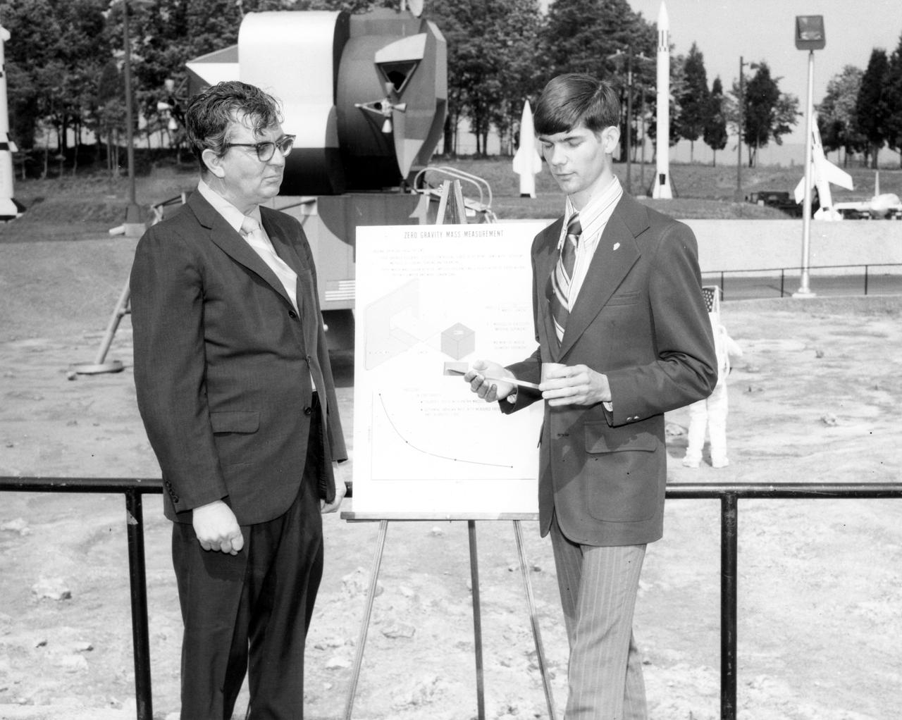 Vincent W. Converse, high school student from Rockford, Illinois, discussed a mass measurement device he proposed for the Skylab mission with Dr. Robert Head of the Marshall Space Flight Center (MSFC) during his visit to the center.  The lunar surface scene in the background is one of many space exhibits at the Alabama Space and Rocket Center in nearby Huntsville, Alabama. Converse was among 25 winners of a contest in which some 3,500 high school students proposed experiments for the following year’s Skylab mission. The nationwide scientific competition was sponsored by the National Science Teachers Association and the National Aeronautics and Space Administration (NASA). The winning students, along with their parents and sponsor teachers, visited MSFC where they met with scientists and engineers, participated in design reviews for their experiments, and toured MSFC facilities. Of the 25 students, 6 did not see their experiments conducted on Skylab because the experiments were not compatible with Skylab hardware and timelines. Of the 19 remaining, 11 experiments required the manufacture of additional equipment. 