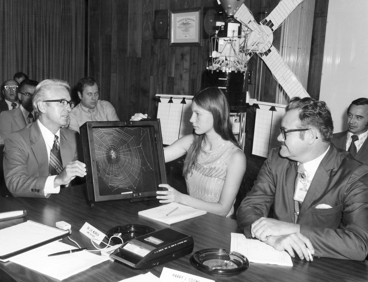 Lexington, Massachusetts high school student, Judith Miles, discusses her proposed Skylab experiment with Keith Demorest (right) and Henry Floyd, both of Marshall Space Flight Center (MSFC). In her experiment, called the “Web Formation in Zero Gravity”, called for spiders to be released into a box and their actions recorded to determine how well they adapt to the absence of gravity. Spiders are known to adapt quickly to other changes in the environment but nothing was known of their ability to adapt to weightlessness.  At the same time spiders were weaving webs in Earth orbit, similar spiders were spinning webs in identical boxes on Earth under full gravity conditions. Miles was among the 25 winners of a contest in which some 3,500 high school students proposed experiments for the following year’s Skylab Mission. Of the 25 students, 6 did not see their experiments conducted on Skylab because the experiments were not compatible with Skylab hardware and timelines. Of the 19 remaining, 11 experiments required the manufacture of equipment.