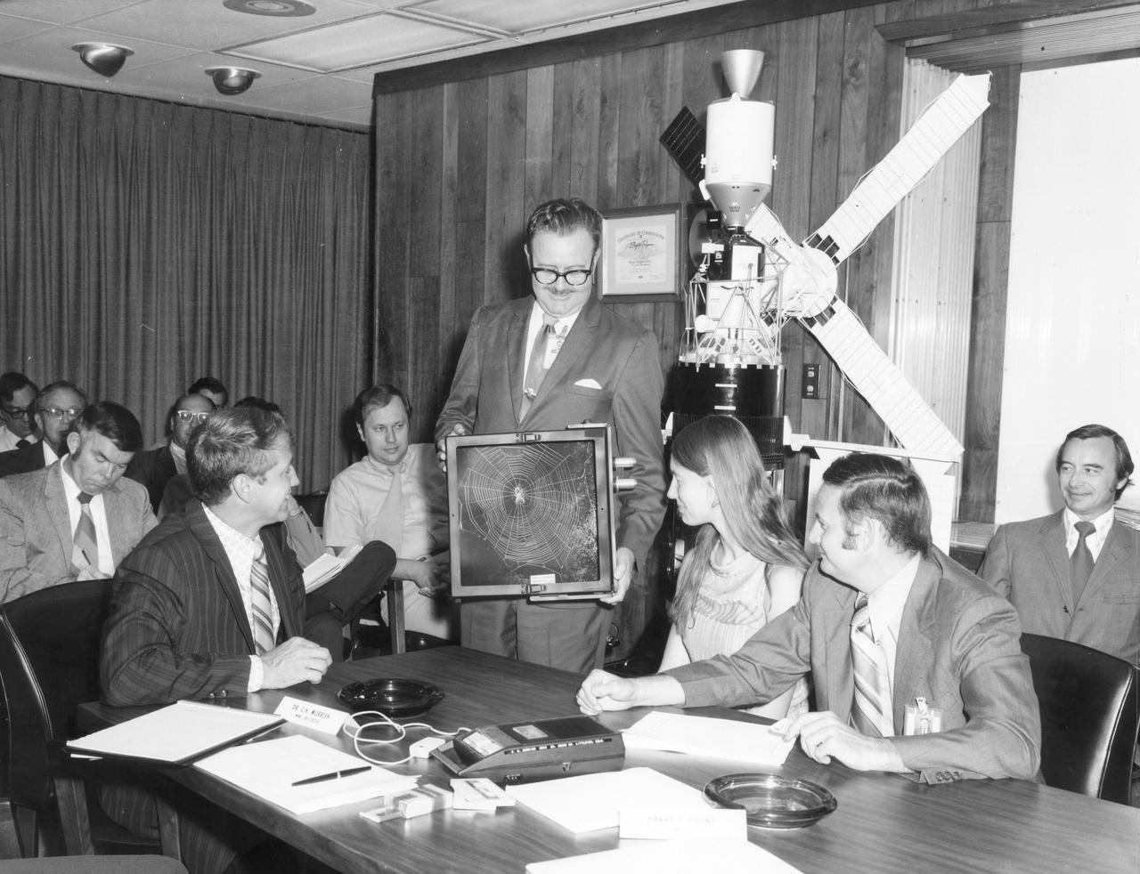Lexington, Massachusetts high school student, Judith Miles, discusses her proposed Skylab experiment with engineers and scientists during a design review of the experiment equipment.  At left is Ron Pavlue of Kennedy Space Flight Center (KSC), holding a box is Keith Demorest of Marshall Space Flight Center (MSFC). Right of Miles is Dr. Raymond Gause, also of MSFC, who is Miles’ scientific advisor. In her experiment, called the “Web Formation in Zero Gravity”, spiders were released into a box and their actions recorded to determine how well they adapt to the absence of gravity. Spiders are known to adapt quickly to other changes in the environment but nothing was known of their ability to adapt to weightlessness.  At the same time spiders were weaving webs in Earth orbit, similar spiders were spinning webs in identical boxes on Earth under full gravity conditions. Miles was among the 25 winners of a contest in which some 3,500 high school students proposed experiments for the following year’s Skylab mission. Of the 25 students, 6 did not see their experiments conducted on Skylab because the experiments were not compatible with Skylab hardware and timelines. Of the 19 remaining, 11 experiments required the manufacture of equipment.