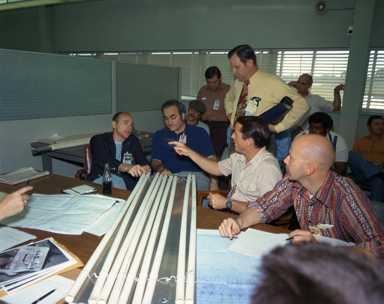 Sixty-three seconds after the launch of the modified Saturn V vehicle carrying the Skylab cluster, engineers in the operation support and control center saw an unexpected telemetry indication that signalled that damages occurred on one solar array and the micrometeoroid shield during the launch. Still unoccupied, the Skylab was stricken with the loss of the heat shield and sunlight beat mercilessly on the lab's sensitive skin. Internal temperatures soared, rendering the the station uninhabitable, threatening foods, medicines, films, and experiments. The launch of the first marned Skylab (Skylab-2) mission was delayed until methods were devised to repair and salvage the workshop. Personnel from other NASA Centers and industries quickly joined the Marshall Space Flight Center (MSFC) in efforts to save the damaged Skylab. They worked day and night for the next several days. Eventually the MSFC developed, tested, rehearsed, and approved three repair options. These options included a parasol sunshade and a twin-pole sunshade to restore the temperature inside the workshop, and a set of metal cutting tools to free the jammed solar panel. This photograph was taken during a discussion of the methods of the twin-pole Sun shield by (left to right) Astronaut Alan Bean, MSFC Director Dr. Rocco Petrone, Astronaut Edward Gibson, and MSFC engineer Richard Heckman. Dr. William Lucas, who became MSFC Director after Dr. Petrone left MSFC in March of 1974, is standing.