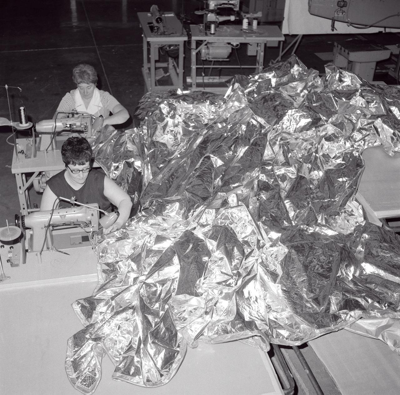 Two seamstresses stitch together a sun-shade for Skylab Orbital Workshop (OWS), the first U.S. experimental space station in orbit, which lost its thermal protection shield during the launch on May 14, 1973. Without the heat shield, the temperature inside the Orbital Workshop became dangerously high, rendering the workshop uninhabitable and threatened deterioration of the interior insulation and adhesive. Engineers and scientists at Marshall Space Flight Center (MSFC) worked tirelessly around the clock on the emergency repair procedure. The Skylab crew and the repair kits were launched just 11 days after the incident. The crew successfully deployed the twin-pole sail parasol sun-shade during their EVA (Extravehicular Activity) the next day. 