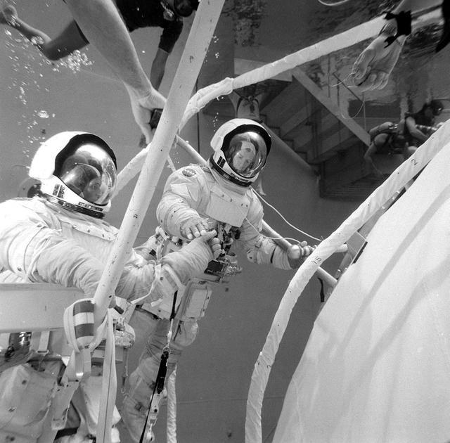 This photograph was taken during testing of an emergency procedure to free jammed solar array panels on the Skylab workshop. A metal strap became tangled over one of the folded solar array panels when Skylab lost its micrometeoroid shield during the launch. This photograph shows astronauts Schweickart and Gibson in the Marshall Space Flight Center (MSFC) Neutral Buoyancy Simulator (NBS) using various cutting tools and methods developed by the MSFC to free the jammed solar wing. Extensive testing and many hours of practice in simulators such as the NBS tank helped prepare the Skylab crewmen for extravehicular performance in the weightless environment. This huge water tank simulated the weightless environment that the astronauts would encounter in space.