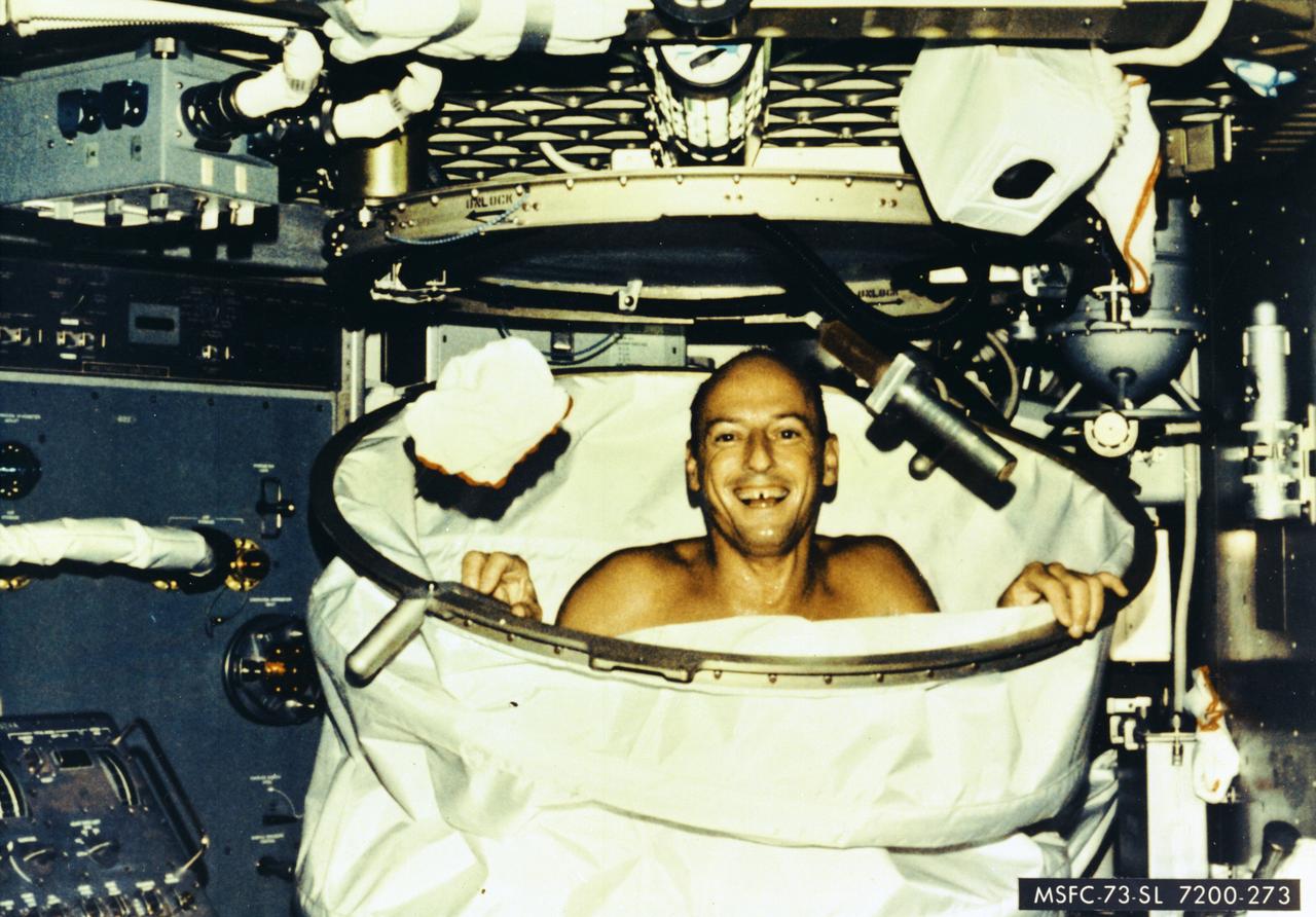 Astronaut Charles Conrad, Jr., Skylab-2 (SL-2) commander, smiles happily for the camera after a hot bath in the shower in the crew quarters of the Orbital Workshop of the Skylab space station.  In deploying the shower facility, the shower curtain was pulled up from the floor and attached to the ceiling.  The water came through a push button shower head attached to a flexible hose. Water was drawn off by a vacuum system.