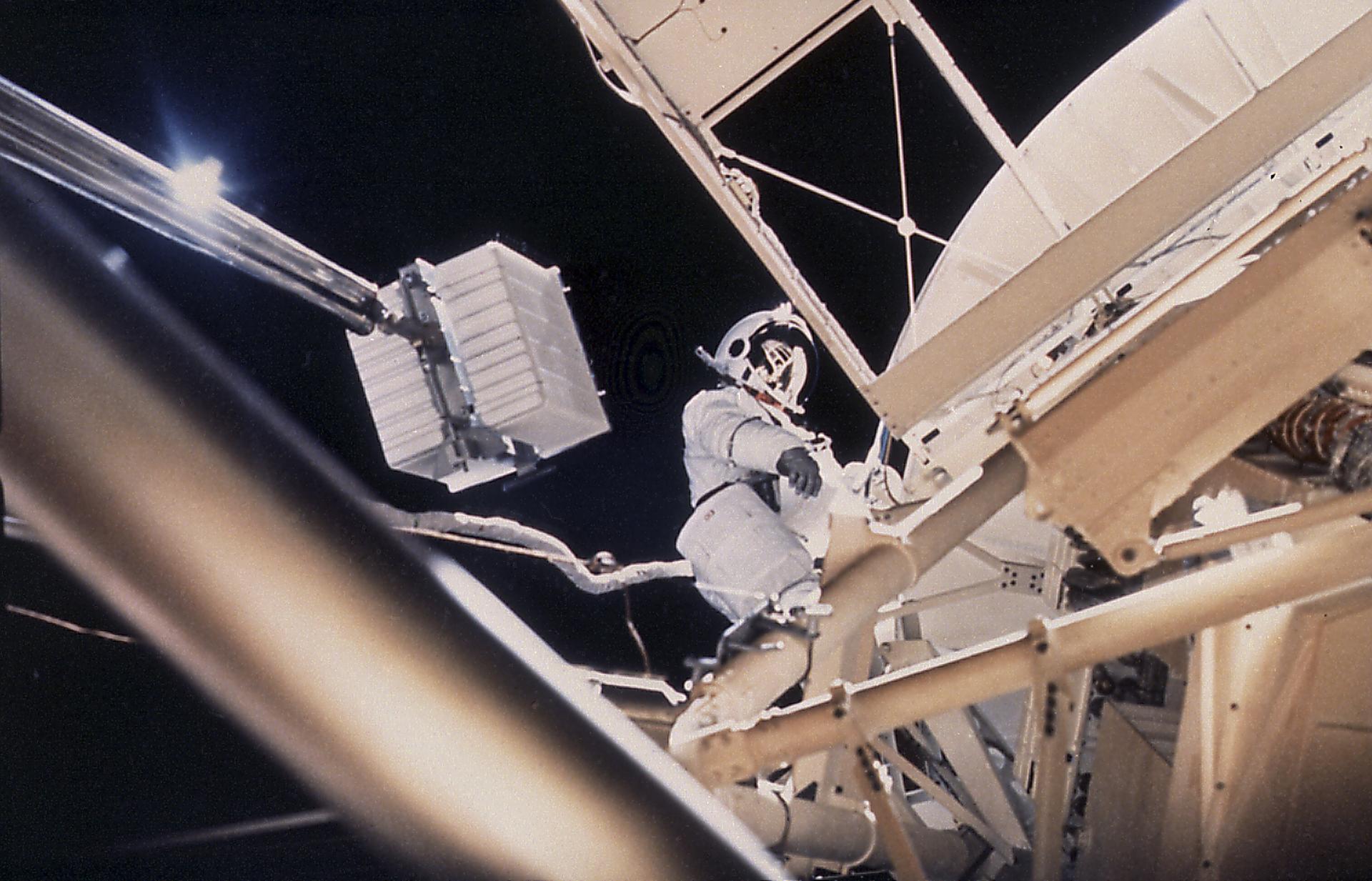 This onboard photograph depicts Astronaut Owen Garriott atop the Apollo Telescope Mount, removing a film magazine (white box) from one of Skylab's solar telescopes during an Extravehicular Activity (EVA)