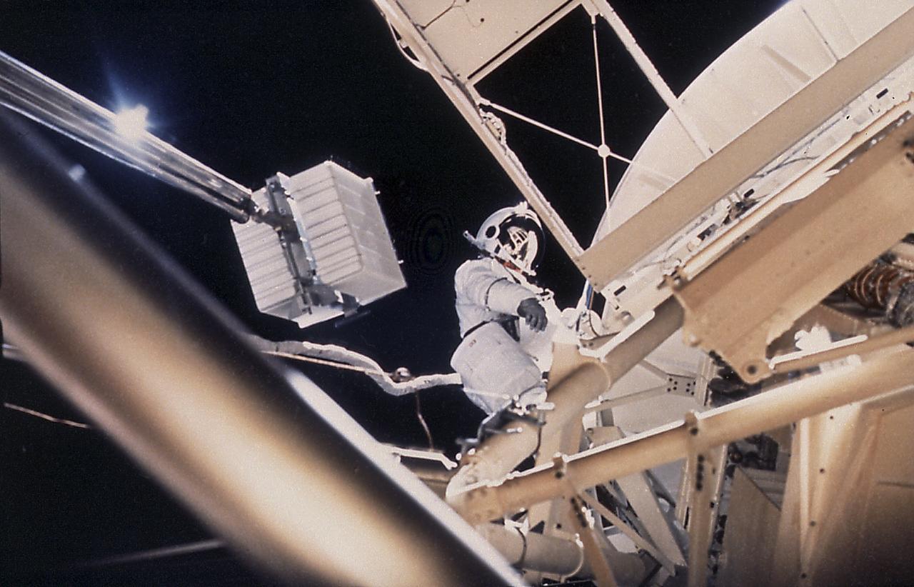 This onboard photograph depicts Astronaut Owen Garriott atop the Apollo Telescope Mount, removing a film magazine (white box) from one of Skylab's solar telescopes during an Extravehicular Activity (EVA) in the second marned Skylab mission (Skylab-3). A long boom transported it back into the waiting hands of another crew member at the airlock door below. During the operation, Garriott, film, boom, and Skylab were 435 kilometers high and speeding around the Earth at 29,000 kilometers per/hour. Because they moved together with no wind resistance, there was little sense of motion. 