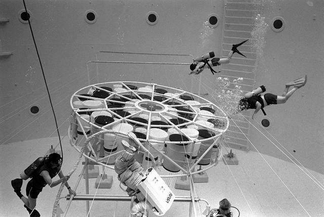 Once the United States' space program had progressed from Earth's orbit into outerspace, the prospect of building and maintaining a permanent presence in space was realized. To accomplish this feat, NASA launched a temporary workstation, Skylab, to discover the effects of low gravity and weightlessness on the human body, and also to develop tools and equipment that would be needed in the future to build and maintain a more permanent space station. The structures, techniques, and work schedules had to be carefully designed to fit this unique construction site. The components had to be lightweight for transport into orbit, yet durable. The station also had to be made with removable parts for easy servicing and repairs by astronauts. All of the tools necessary for service and repairs had to be designed for easy manipulation by a suited astronaut. And construction methods had to be efficient due to limited time the astronauts could remain outside their controlled environment. In lieu of all the specific needs for this project, an environment on Earth had to be developed that could simulate a low gravity atmosphere. A Neutral Buoyancy Simulator (NBS) was constructed by NASA Marshall Space Flight Center (MSFC) in 1968. Since then, NASA scientists have used this facility to understand how humans work best in low gravity and also provide information about the different kinds of structures that can be built.Pictured is an experiment where the astronaut is required to move a large object which weighed 19,000 pounds. It was moved with realitive ease once the astronaut became familiar with his environment and his near weightless condition. Experiments of this nature provided scientists with the information needed regarding weight and mass allowances astronauts could manage in preparation for building a permanent space station in the future.