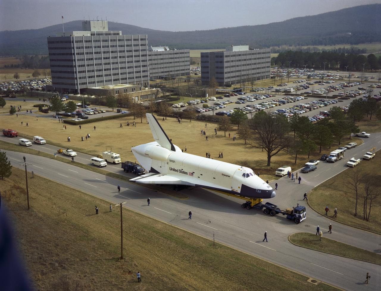 In this view, the Shuttle Orbiter Enterprise is seen heading South on Rideout Road with Marshall Space Flight Center's (MSFC'S) administrative 4200 Complex in the background, as it is being transported to MSFC's building 4755 for later Mated Vertical Ground Vibration tests (MVGVT) at MSFC's Dynamic Test Stand. The tests marked the first time ever that the entire shuttle complement (including Orbiter, external tank, and solid rocket boosters) were mated vertically.