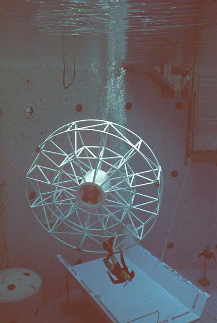 Once the United States' space program had progressed from Earth's orbit into outerspace, the prospect of building and maintaining a permanent presence in space was realized. To accomplish this feat, NASA launched a temporary workstation, Skylab, to discover the effects of low gravity and weightlessness on the human body, and also to develop tools and equipment that would be needed in the future to build and maintain a more permanent space station. The structures, techniques, and work schedules had to be carefully designed to fit this unique construction site. The components had to be lightweight for transport into orbit, yet durable. The station also had to be made with removable parts for easy servicing and repairs by astronauts. All of the tools necessary for service and repairs had to be designed for easy manipulation by a suited astronaut. And construction methods had to be efficient due to limited time the astronauts could remain outside their controlled environment. In lieu of all the specific needs for this project, an environment on Earth had to be developed that could simulate a low gravity atmosphere. A Neutral Buoyancy Simulator (NBS) was constructed by NASA Marshall Space Flight Center (MSFC) in 1968. Since then, NASA scientists have used this facility to understand how humans work best in low gravity and also provide information about the different kinds of structures that can be built. Included in the plans for the space station was a space telescope. This telescope would be attached to the space station and directed towards outerspace. Astronomers hoped that the space telescope would provide a look at space that is impossible to see from Earth because of Earth's atmosphere and other man made influences. Pictured is a large structure that is being used as the antenna base for the space telescope.