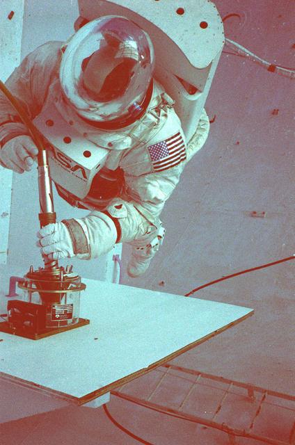 Once the United States' space program had progressed from Earth's orbit into outerspace, the prospect of building and maintaining a permanent presence in space was realized. To accomplish this feat, NASA launched a temporary workstation, Skylab, to discover the effects of low gravity and weightlessness on the human body, and also to develop tools and equipment that would be needed in the future to build and maintain a more permanent space station. The structures, techniques, and work schedules had to be carefully designed to fit this unique construction site. The components had to be lightweight for transport into orbit, yet durable. The station also had to be made with removable parts for easy servicing and repairs by astronauts. All of the tools necessary for service and repairs had to be designed for easy manipulation by a suited astronaut. And construction methods had to be efficient due to limited time the astronauts could remain outside their controlled environment. In lieu of all the specific needs for this project, an environment on Earth had to be developed that could simulate a low gravity atmosphere. A Neutral Buoyancy Simulator (NBS) was constructed by NASA Marshall Space Flight Center (MSFC) in 1968. Since then, NASA scientists have used this facility to understand how humans work best in low gravity and also provide information about the different kinds of structures that can be built. Another facet of the space station would be electrical cornectors which would be used for powering tools the astronauts would need for construction, maintenance and repairs. Shown is an astronaut training during an underwater electrical connector test in the NBS.