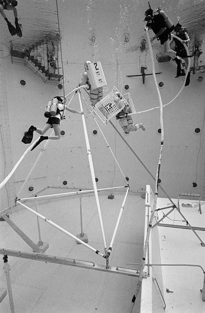 Once the United States' space program had progressed from Earth's orbit into outerspace, the prospect of building and maintaining a permanent presence in space was realized. To accomplish this feat, NASA launched a temporary workstation, Skylab, to discover the effects of low gravity and weightlessness on the human body, and also to develop tools and equipment that would be needed in the future to build and maintain a more permanent space station. The structures, techniques, and work schedules had to be carefully designed to fit this unique construction site. The components had to be lightweight for transport into orbit, yet durable. The station also had to be made with removable parts for easy servicing and repairs by astronauts. All of the tools necessary for service and repairs had to be designed for easy manipulation by a suited astronaut. And construction methods had to be efficient due to limited time the astronauts could remain outside their controlled environment. In lieu of all the specific needs for this project, an environment on Earth had to be developed that could simulate a low gravity atmosphere. A Neutral Buoyancy Simulator (NBS) was constructed by NASA Marshall Space Flight Center (MSFC) in 1968. Since then, NASA scientists have used this facility to understand how humans work best in low gravity and also provide information about the different kinds of structures that can be built. With the help of the NBS, building a space station became more of a reality. In a joint venture between NASA/Langley Research Center in Hampton, VA and MSFC, the Assembly Concept for Construction of Erectable Space Structures (ACCESS) was developed and demonstrated at MSFC's NBS. The primary objective of this experiment was to test the ACCESS structural assembly concept for suitability as the framework for larger space structures and to identify ways to improve the productivity of space construction. Pictured is a demonstration of ACCESS.