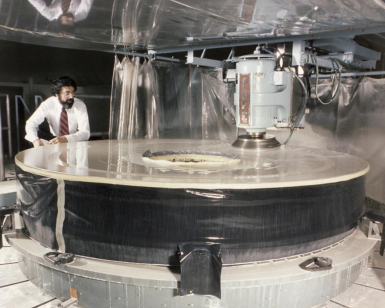 This photograph shows the Hubble Space Telescope's (HST's) Primary Mirror being ground at the Perkin-Elmer Corporation's large optics fabrication facility. After the 8-foot diameter mirror was ground to shape and polished, the glass surface was coated with a reflective layer of aluminum and a protective layer of magnesium fluoride, 0.1- and 0.025-micrometers thick, respectively. The purpose of the HST, the most complex and sensitive optical telescope ever made, is to study the cosmos from a low-Earth orbit. By placing the telescope in space, astronomers are able to collect data that is free of the Earth's atmosphere. The Marshall Space Flight Center had responsibility for design, development, and construction of the HST and the Perkin-Elmer Corporation, in Danbury, Cornecticut, developed the optical system and guidance sensors.