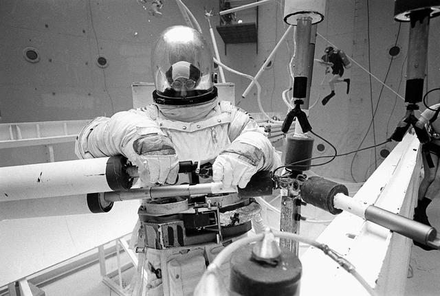 Once the United States' space program had progressed from Earth's orbit into outerspace, the prospect of building and maintaining a permanent presence in space was realized. To accomplish this feat, NASA launched a temporary workstation, Skylab, to discover the effects of low gravity and weightlessness on the human body, and also to develop tools and equipment that would be needed in the future to build and maintain a more permanent space station. The structures, techniques, and work schedules had to be carefully designed to fit this unique construction site. The components had to be lightweight for transport into orbit, yet durable. The station also had to be made with removable parts for easy servicing and repairs by astronauts. All of the tools necessary for service and repairs had to be designed for easy manipulation by a suited astronaut. Construction methods had to be efficient due to the limited time the astronauts could remain outside their controlled environment. In lieu of all the specific needs for this project, an environment on Earth had to be developed that could simulate a low gravity atmosphere. A Neutral Buoyancy Simulator (NBS) was constructed by NASA's Marshall Space Flight Center (MSFC) in 1968. Since then, NASA scientists have used this facility to understand how humans work best in low gravity and also provide information about the different kinds of structures that can be built. Pictured is a Massachusetts Institute of Technology (MIT) student working in a spacesuit on the Experimental Assembly of Structures in Extravehicular Activity (EASE) project which was developed as a joint effort between MFSC and MIT. The EASE experiment required that crew members assemble small components to form larger components, working from the payload bay of the space shuttle. The MIT student in this photo is assembling two six-beam tetrahedrons.