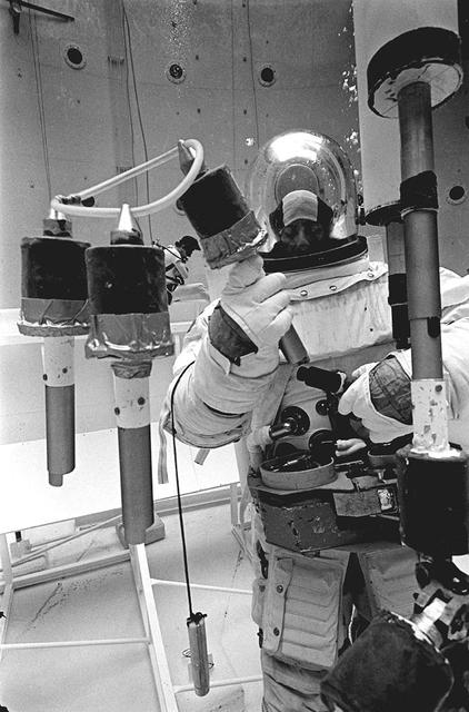 Once the United States' space program had progressed from Earth's orbit into outerspace, theprospect of building and maintaining a permanent presence in space was realized. To accomplish this feat, NASA launched a temporary workstation, Skylab, to discover the effects of low gravity and weightlessness on the human body, and also to develop tools and equipment that would be needed in the future to build and maintain a more permanent space station. The structures, techniques, and work schedules had to be carefully designed to fit this unique construction site. The components had to be lightweight for transport into orbit, yet durable. The station also had to be made with removable parts for easy servicing and repairs by astronauts. All of the tools necessary for service and repairs had to be designed for easy manipulation by a suited astronaut. Construction methods had to be efficient due to the limited time the astronauts could remain outside their controlled environment. In lieu of all the specific needs for this project, an environment on Earth had to be developed that could simulate a low gravity atmosphere. A Neutral Buoyancy Simulator (NBS) was constructed by NASA's Marshall Space Flight Center (MSFC) in 1968. Since then, NASA scientists have used this facility to understand how humans work best in low gravity and also provide information about the different kinds of structures that can be built. Pictured is a Massachusetts Institute of Technology (MIT) student working in a spacesuit on the Experimental Assembly of Structures in Extravehicular Activity (EASE) project which was developed as a joint effort between MFSC and MIT. The EASE experiment required that crew members assemble small components to form larger components, working from the payload bay of the space shuttle. The MIT student in this photo is assembling two six-beam tetrahedrons.