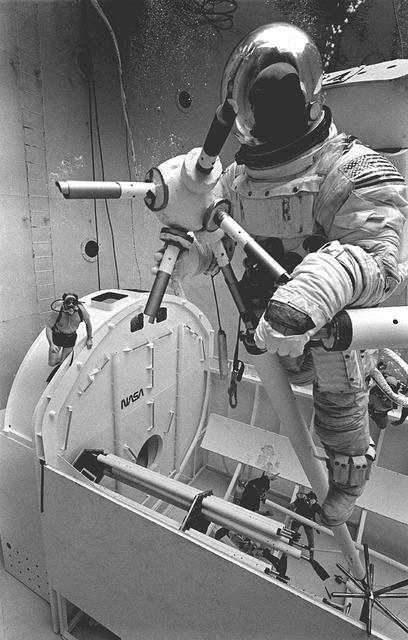 Once the United States' space program had progressed from Earth's orbit into outerspace, the prospect of building and maintaining a permanent presence in space was realized. To accomplish this feat, NASA launched a temporary workstation, Skylab, to discover the effects of low gravity and weightlessness on the human body, and also to develop tools and equipment that would be needed in the future to build and maintain a more permanent space station. The structures, techniques, and work schedules had to be carefully designed to fit this unique construction site. The components had to be lightweight for transport into orbit, yet durable. The station also had to be made with removable parts for easy servicing and repairs by astronauts. All of the tools necessary for service and repairs had to be designed for easy manipulation by a suited astronaut. Construction methods had to be efficient due to the limited time the astronauts could remain outside their controlled environment. In lieu of all the specific needs for this project, an environment on Earth had to be developed that could simulate a low gravity atmosphere. A Neutral Buoyancy Simulator (NBS) was constructed by NASA's Marshall Space Flight Center (MSFC) in 1968. Since then, NASA scientists have used this facility to understand how humans work best in low gravity and also provide information about the different kinds of structures that can be built. Pictured is a Massachusetts Institute of Technology (MIT) student working in a spacesuit on the Experimental Assembly of Structures in Extravehicular Activity (EASE) project which was developed as a joint effort between MFSC and MIT. The EASE experiment required that crew members assemble small components to form larger components, working from the payload bay of the space shuttle. The MIT student in this photo is assembling two six-beam tetrahedrons.