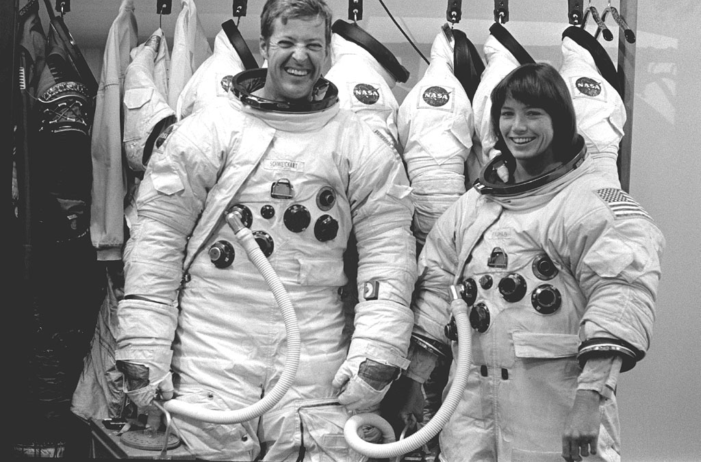 Joe Kerwin (left) and Anna Fisher smile while wearing EVA spacesuits