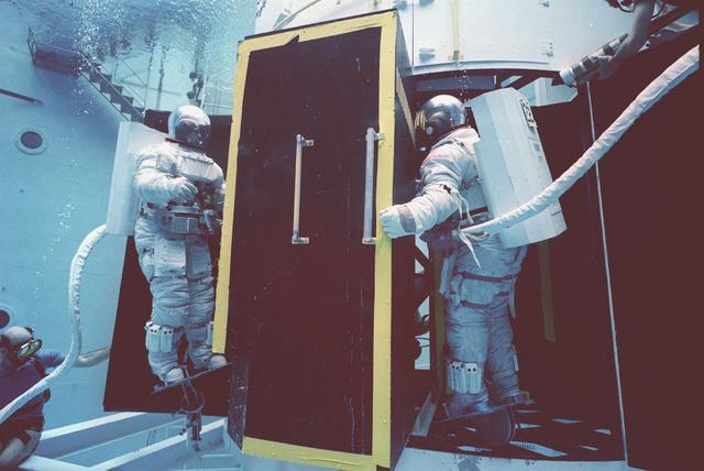 The Hubble Space Telescope (HST) is a cooperative program of the European Space Agency (ESA) and the National Aeronautical and Space Administration (NASA) to operate a long-lived space-based observatory. It was the flagship mission of NASA's Great Observatories program. The HST program began as an astronomical dream in the 1940s. During the 1970s and 1980s, the HST was finally designed and built becoming operational in the 1990s. The HST was deployed into a low-Earth orbit on April 25, 1990 from the cargo bay of the Space Shuttle Discovery (STS-31). The design of the HST took into consideration its length of service and the necessity of repairs and equipment replacement by making the body modular. In doing so, subsequent shuttle missions could recover the HST, replace faulty or obsolete parts and be re-released. Pictured is Marshall Space Flight Center's (MSFC's) Neutral Buoyancy Simulator (NBS) that served as the test center for shuttle astronauts training for Hubble related missions. Shown are astronauts Arna Fisher and Joe Kerwin training on a mock-up of a modular section of the HST for an axial scientific instrument changeout.