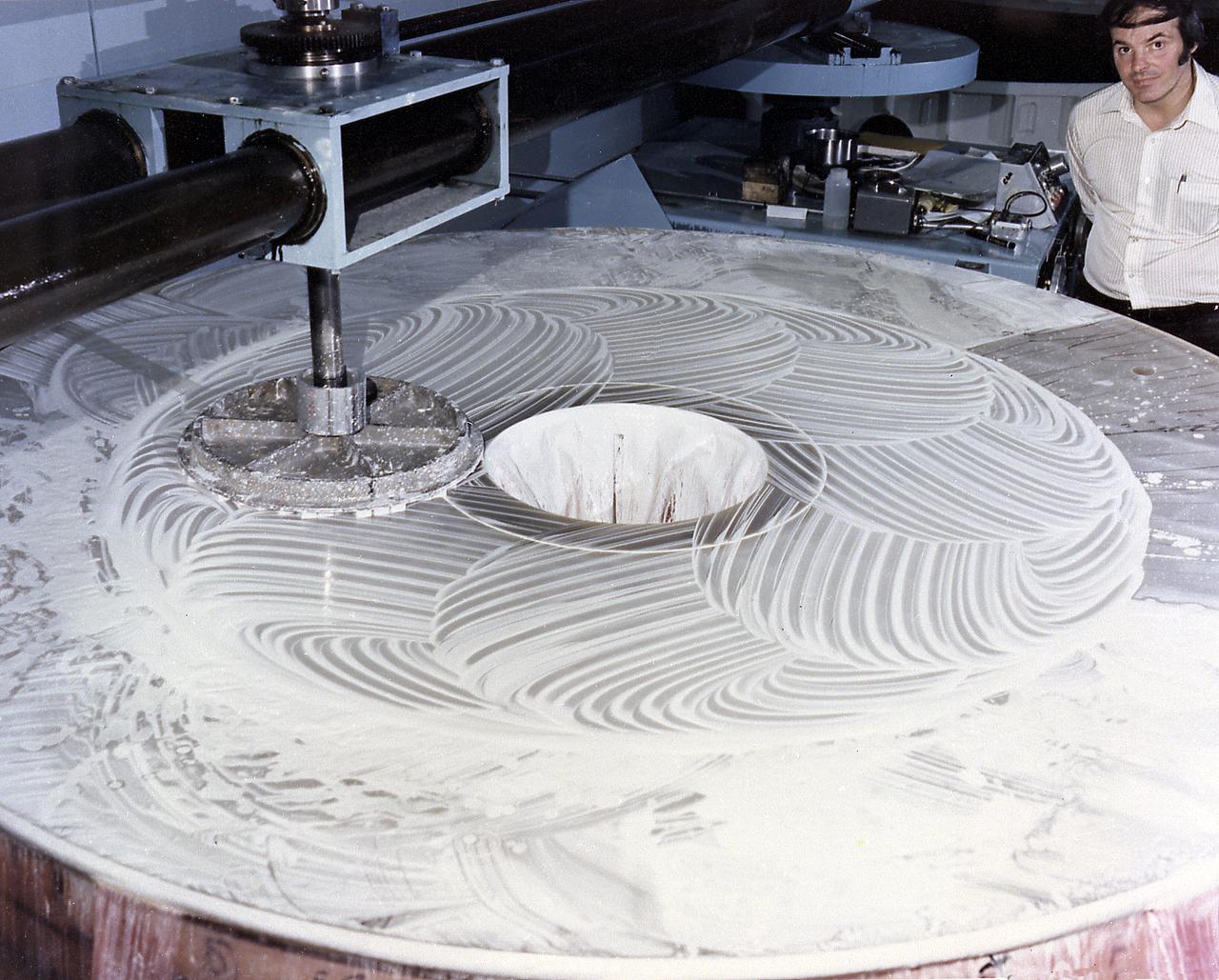 This photograph shows the Hubble Space Telescope's (HST's) Primary Mirror being polished at the the Perkin-Elmer Corporation's large optics fabrication facility. After the 8-foot diameter mirror was ground to shape and polished, the glass surface was coated with a reflective layer of aluminum and a protective layer of magnesium fluoride, 0.1- and 0.025-micrometers thick, respectively. The purpose of the HST, the most complex and sensitive optical telescope ever made, is to study the cosmos from a low-Earth orbit. By placing the telescope in space, astronomers are able to collect data that is free of the Earth's atmosphere. The Marshall Space Flight Center had responsibility for design, development, and construction of the HST and the Perkin-Elmer Corporation, in Danbury, Cornecticut, developed the optical system and guidance sensors.