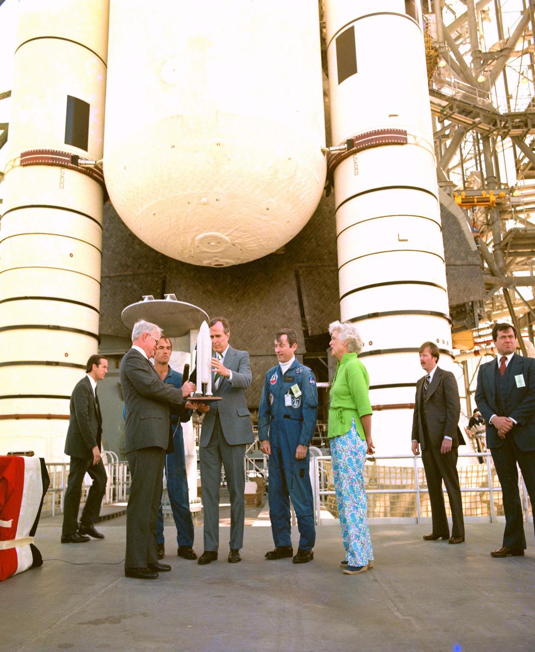KENNEDY SPACE CENTER, FLA. -- Vice President George H. W. Bush, center, flanked by astronauts Robert L. Crippen on his right and John W. Young on his left, receives a model of the Space Shuttle from Dr. Alan M. Lovelace, acting administrator of the National Aeronautics and Space Administration. At far right is Mrs. Bush, who accompanied the vice president on his whirlwind tour of the Shuttle vehicle and launch facilities. In the background are the aft portions of the orbiter, external tank and solid rocket boosters. The Shuttle, America's first reusable space transportation system, is scheduled to make its maiden voyage into space no sooner than the week of April 7.
