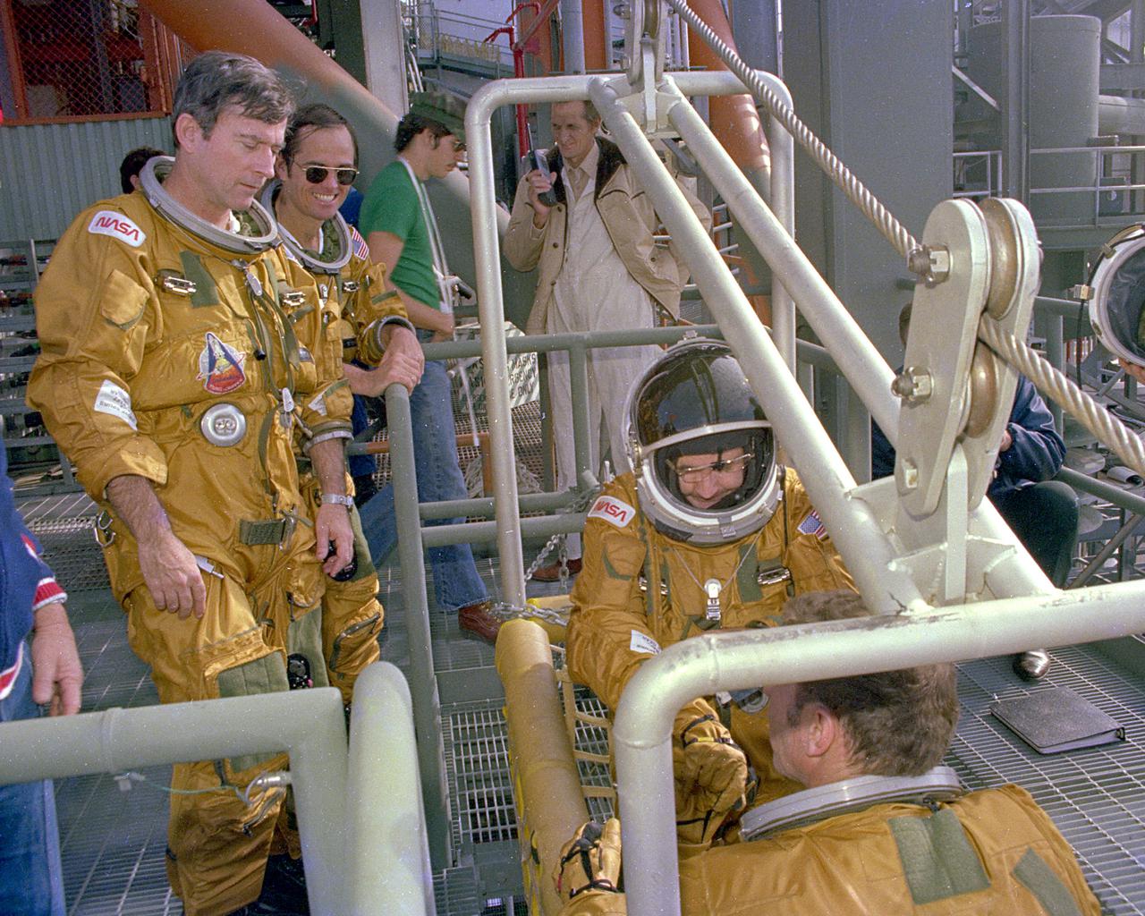 KENNEDY SPACE CENTER, FLA. -  Space Shuttle prime crew Commander John Young and Pilot Bob Crippen watch as backup crew members Richard Truly and Joe Engle board the emergency pad escape system known as the slidewire.  The slidewire system provides a quick escape from upper launch pad platforms in case of a serious emergency.  The flight crews wore the spacesuits and other equipment to be worn during a mission, but sandbags were used to duplicate the weight of riders in the slidewire baskeets during the training.