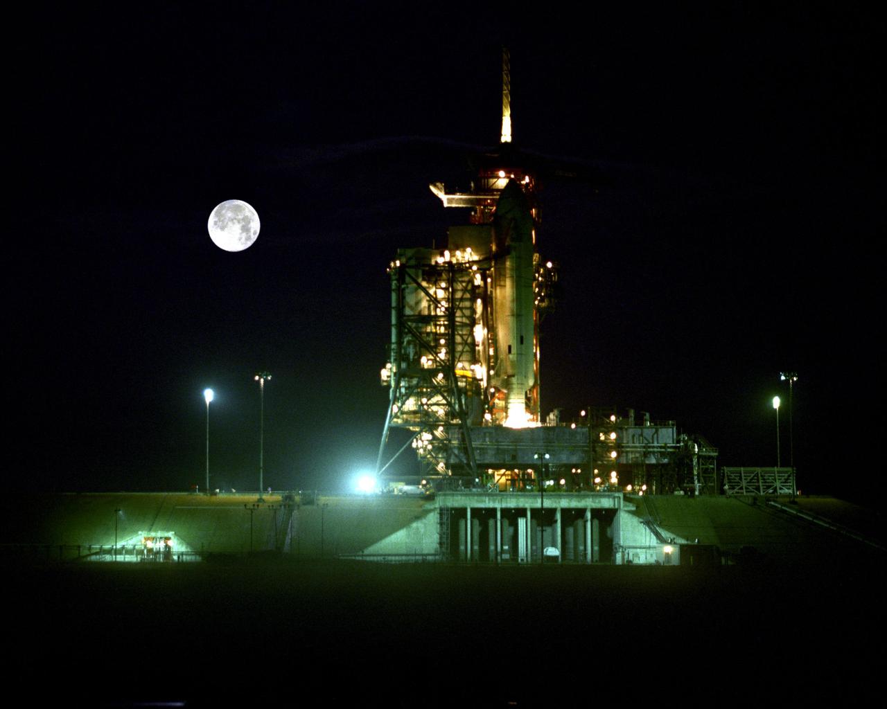 KENNEDY SPACE CENTER, FLA. - Looking like the perfect staging for a science fiction movie, STS-1 is a dramatic companion for the Moon 'over its shoulder.' The Space Shuttle, comprised of the orbiter Columbia, the external tank and two solid rocket boosters, is pictured during final preparations for Flight Readiness Firing of the orbiter's main engines, a landmark test during launch preparations.
