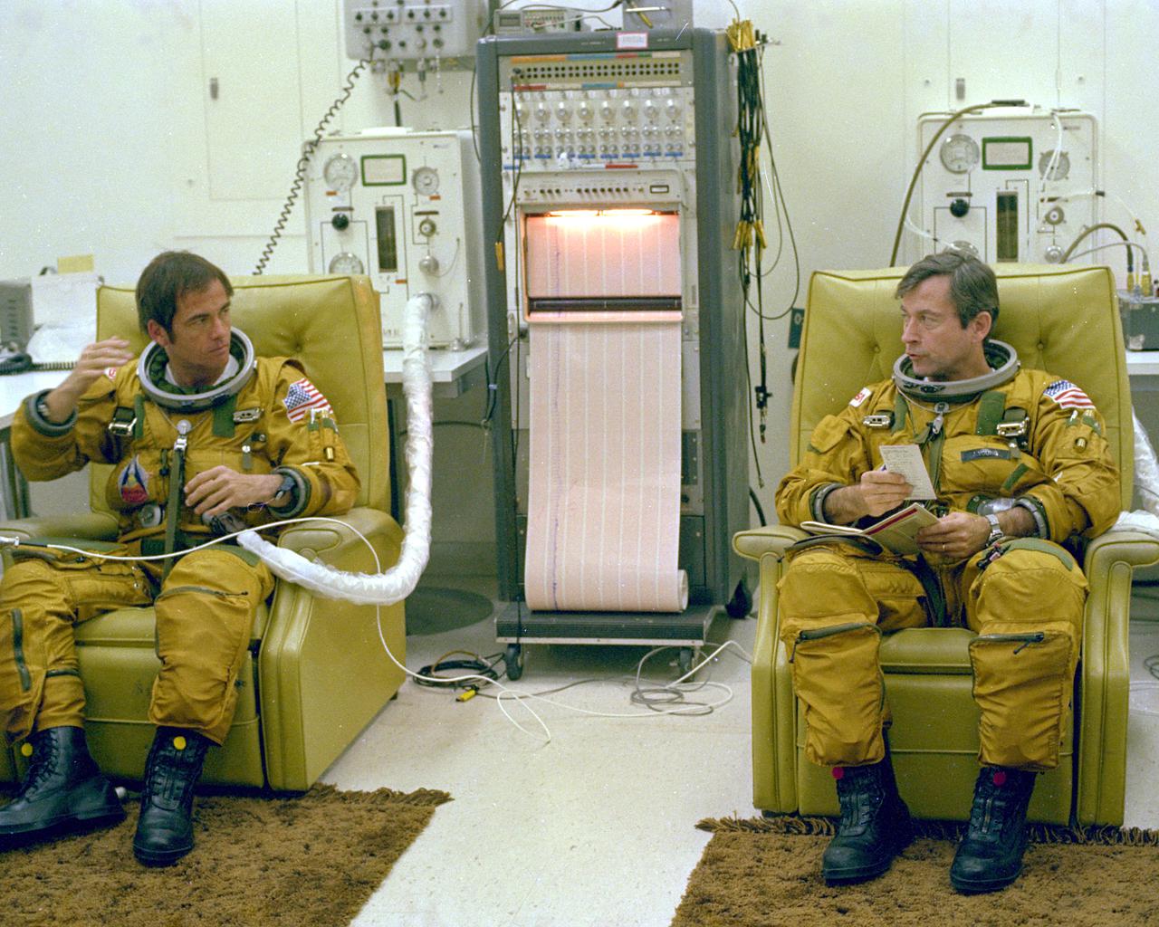 KENNEDY SPACE CENTER, FLA. - Prime crew astronauts Bob Crippen (left) and John Young (right) discuss checklist items during suit-up in the Operations and Checkout Building iiror to departure for the launch pad during the final countdown rehearsal before launch of STS-1.