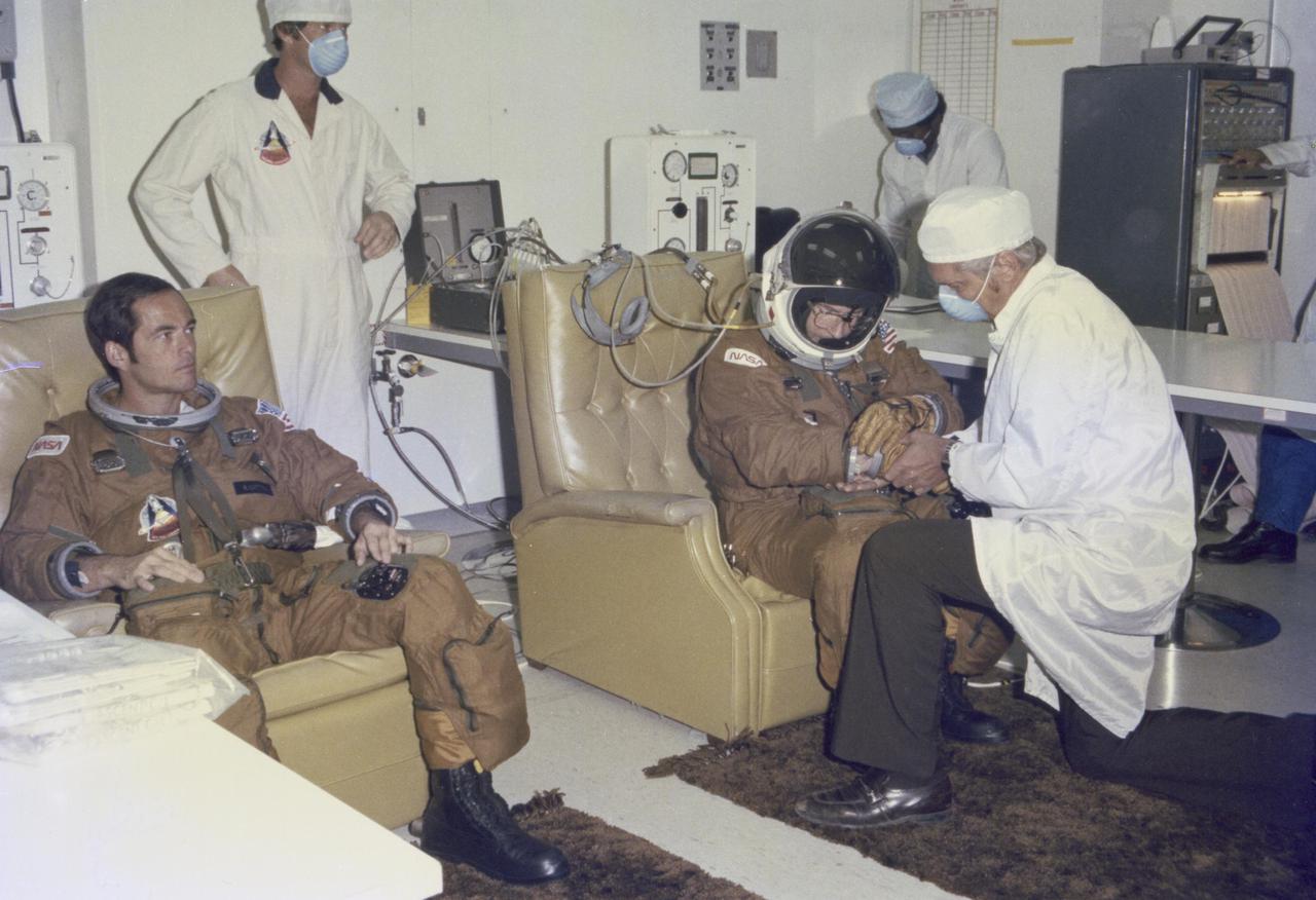 KENNEDY SPACE CENTER, FLA. -- Technicians assist prime crew Astronauts Bob Crippen (left) and John Young (right) in suit-up operations in KSC’s Operations and Checkout Building on the morning of Columbia’s successful liftoff on the Space Shuttle’s first orbital flight. Crippen is the pilot and Young is the commander for mission STS-1 aboard Space Shuttle Columbia. The STS-1 mission, known as a shuttle systems test flight, seeks to demonstrate safe launch into orbit and safe return of the orbiter and crew and verify the combined performance of the entire shuttle vehicle -- orbiter, solid rocket boosters and external tank.