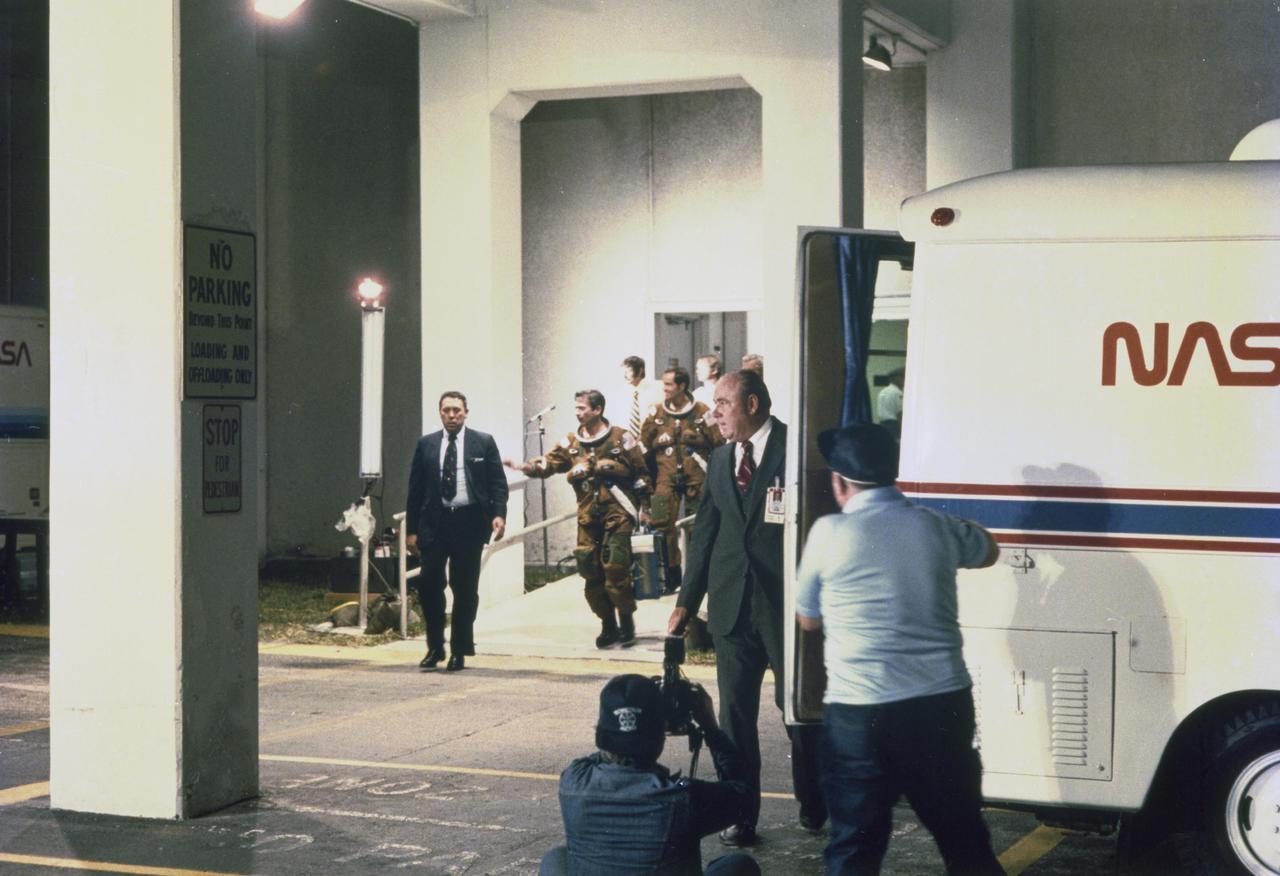 KENNEDY SPACE CENTER, FLA.  -  Space flight-suited Astronauts John Young, left, and Robert Crippen, accompanied by George Abbey, at far left, flight operations director, Johnson Space Center, walk from the Operations and Checkout Building to the transport van that will take them to Launch Pad 39A, for the first launch of the Space Shuttle at 7 a.m., April 12.  At the rear door of the van is Charles Buckley, head of the security office, KSC. The STS-1 mission, known as a shuttle systems test flight, will seek to demonstrate safe launch into orbit and safe return of the orbiter and crew and verify the combined performance of the entire shuttle vehicle -- orbiter, solid rocket boosters and external tank.