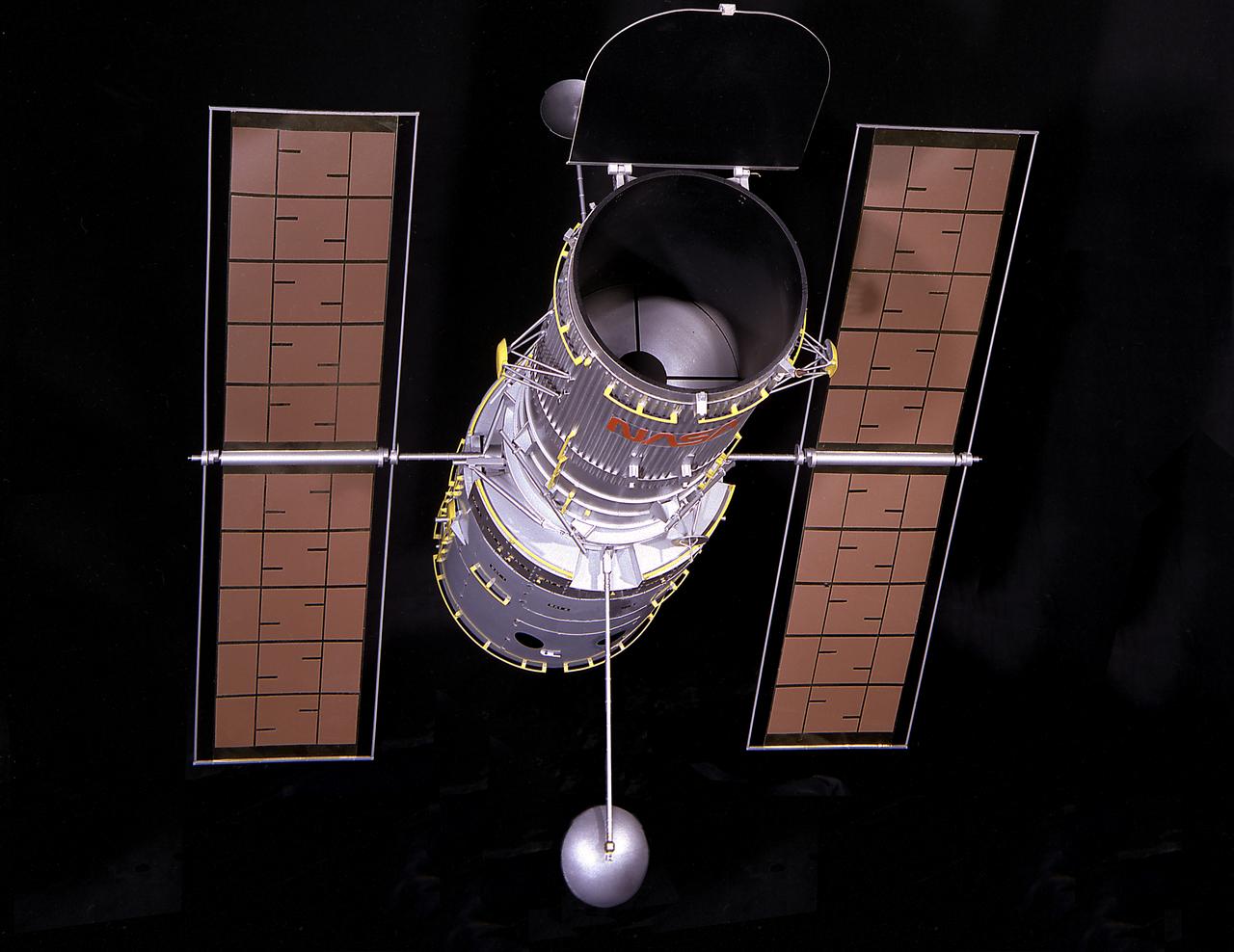 This is a photograph of a 1/15 scale model of the Hubble Space Telescope (HST). The HST is the product of a partnership between NASA, European Space Agency Contractors, and the international community of astronomers. It is named after Edwin P. Hubble, an American Astronomer who discovered the expanding nature of the universe and was the first to realize the true nature of galaxies. The purpose of the HST, the most complex and sensitive optical telescope ever made, is to study the cosmos from a low-Earth orbit. By placing the telescope in space, astronomers are able to collect data that is free of the Earth's atmosphere. The HST detects objects 25 times fainter than the dimmest objects seen from Earth and provides astronomers with an observable universe 250 times larger than visible from ground-based telescopes, perhaps as far away as 14 billion light-years. The HST views galaxies, stars, planets, comets, possibly other solar systems, and even unusual phenomena such as quasars, with 10 times the clarity of ground-based telescopes. The major elements of the HST are the Optical Telescope Assembly (OTA), the Support System Module (SSM), and the Scientific Instruments (SI). The HST is 42.5-feet (13- meters) long and weighs about 25,000 pounds (11,600 kilograms). The HST was deployed from the Space Shuttle Discovery (STS-31 mission) into Earth orbit in April 1990. The Marshall Space Flight Center had responsibility for design, development, and construction of the HST. The Perkin-Elmer Corporation, in Danbury, Cornecticut, developed the optical system and guidance sensors. The Lockheed Missile and Space Company of Sunnyvale, California produced the protective outer shroud and spacecraft systems, and assembled and tested the finished telescope.