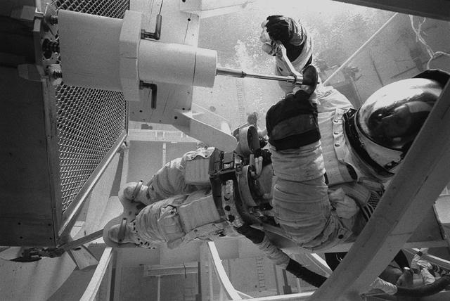 In February 1980, a satellite called Solar Maximum Mission Spacecraft, or Solar Max, was launched into Earth's orbit. Its primary objective was to provide a detailed study of solar flares,active regions on the Sun's surface, sunspots, and other solar activities. Additionally, it was to measure the total output of radiation from the Sun. Not much was known about solar activity at that time except for a slight knowledge of solar flares. After its launch, Solar Max fulfilled everyone's expectations. However, after a year in orbit, Solar Max's Altitude Control System malfunctioned, preventing the precise pointing of instruments at the Sun. NASA scientists were disappointed at the lost data, but not altogether dismayed because Solar Max had been designed for Space Shuttle retrievability enabling the repair of the satellite. On April 6, 1984, Space Shuttle Challenger (STS-41C), Commanded by astronaut Robert L. Crippen and piloted by Francis R. Scobee, launched on a historic voyage. This voyage initiated a series of firsts for NASA; the first satellite retrieval, the first service use of a new space system called the Marned Maneuvering Unit (MMU), the first in-orbit repair, the first use of the Remote Manipulator System (RMS), and the Space Shuttle Challenger's first space flight. The mission was successful in retrieving Solar Max. Mission Specialist Dr. George D. Nelson, using the MMU, left the orbiter's cargo bay and rendezvoused with Solar Max. After attaching himself to the satellite, he awaited the orbiter to maneuver itself nearby. Using the RMS, Solar Max was captured and docked in the cargo bay while Dr. Nelson replaced the altitude control system and the coronagraph/polarimeter electronics box. After the repairs were completed, Solar Max was redeposited in orbit with the assistance of the RMS. Prior to the April 1984 launch, countless man-hours were spent preparing for this mission. The crew of Challenger spent months at Marshall Space Flight Center's (MSFC) Neutral Buoyancy Simulator (NBS) practicing retrieval maneuvers, piloting the MMU, and training on equipment so they could make the needed repairs to Solar Max. Pictured is Dr. Nelson performing a replacement task on the Solar Max mock-up in the NBS.