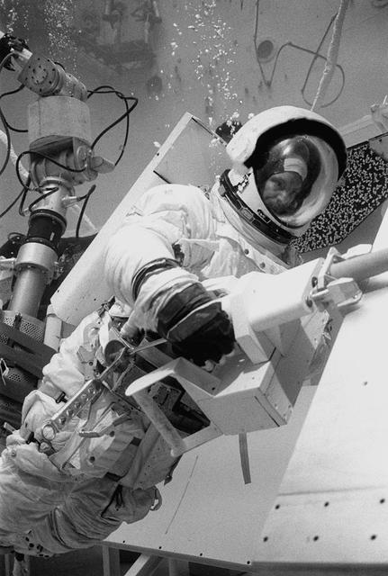 In February 1980, a satellite called Solar Maximum Mission Spacecraft, or Solar Max, was launched into Earth's orbit. Its primary objective was to provide a detailed study of solar flares, active regions on the Sun's surface, sunspots, and other solar activities. Additionally, it was to measure the total output of radiation from the Sun. Not much was known about solar activity at that time except for a slight knowledge of solar flares. After its launch, Solar Max fulfilled everyone's expectations. However, after a year in orbit, Solar Max's Altitude Control System malfunctioned, preventing the precise pointing of instruments at the Sun. NASA scientists were disappointed at the lost data, but not altogether dismayed because Solar Max had been designed for Space Shuttle retrievability enabling repair of the satellite. On April 6, 1984, Space Shuttle Challenger (STS-41C), Commanded by astronaut Robert L. Crippen and piloted by Francis R. Scobee, launched on a historic voyage. This voyage initiated a series of firsts for NASA; the first satellite retrieval, the first service use of a new space system called the Marned Maneuvering Unit (MMU), the first in-orbit repair, the first use of the Remote Manipulator System (RMS), and the Space Shuttle Challenger's first space flight. The mission was successful in retrieving Solar Max. Mission Specialist Dr. George D. Nelson, using the MMU, left the orbiter's cargo bay and rendezvoused with Solar Max. After attaching himself to the satellite, he awaited the orbiter to maneuver itself nearby. Using the RMS, Solar Max was captured and docked in the cargo bay while Dr. Nelson replaced the altitude control system and the coronagraph/polarimeter electronics box. After the repairs were completed, Solar Max was redeposited in orbit with the assistance of the RMS. Prior to the April 1984 launch, countless man-hours were spent preparing for this mission. The crew of Challenger spent months at Marshall Space Flight Center's (MSFC) Neutral Buoyancy Simulator (NBS) practicing retrieval maneuvers, piloting the MMU, and training on equipment so they could make the needed repairs to Solar Max. Pictured is Dr. Nelson performing a replacement task on the Solar Max mock-up in the NBS.