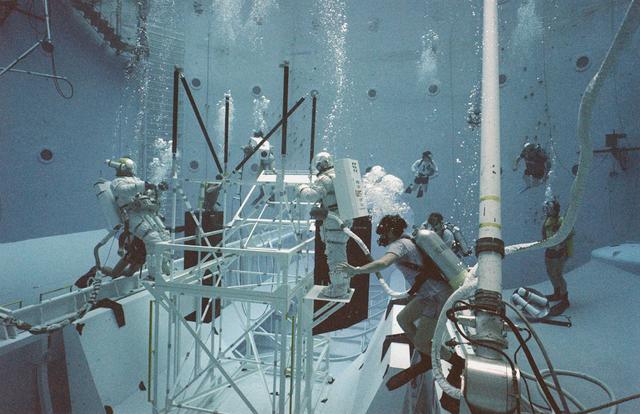 One of the main components of the Hubble Space Telescope (HST) is the Solar Array Drive Electronics (SADE) system. This system interfaces with the Support System Module (SSM) for exchange of operational commands and telemetry data. SADE operates and controls the Solar Array Drive Mechanisms (SADM) for the orientation of the Solar Array Drive (SAD). It also monitors the position of the arrays and the temperature of the SADM. During the first HST servicing mission, the astronauts replaced the SADE component because of some malfunctions. This turned out to be a very challenging extravehicular activity (EVA). Two transistors and two diodes had been thermally stressed with the conformal coating discolored and charred. Soldered cornections became molten and reflowed between the two diodes. The failed transistors gave no indication of defective construction. All repairs were made and the HST was redeposited into orbit. Prior to undertaking this challenging mission, the orbiter's crew trained at Marshall Space Flight Center's (MSFC) Neutral Buoyancy Simulator (NBS) to prepare themselves for working in a low gravity environment. They also practiced replacing HST parts and exercised maneuverability and equipment handling. Pictured are crew members practicing on a space platform.