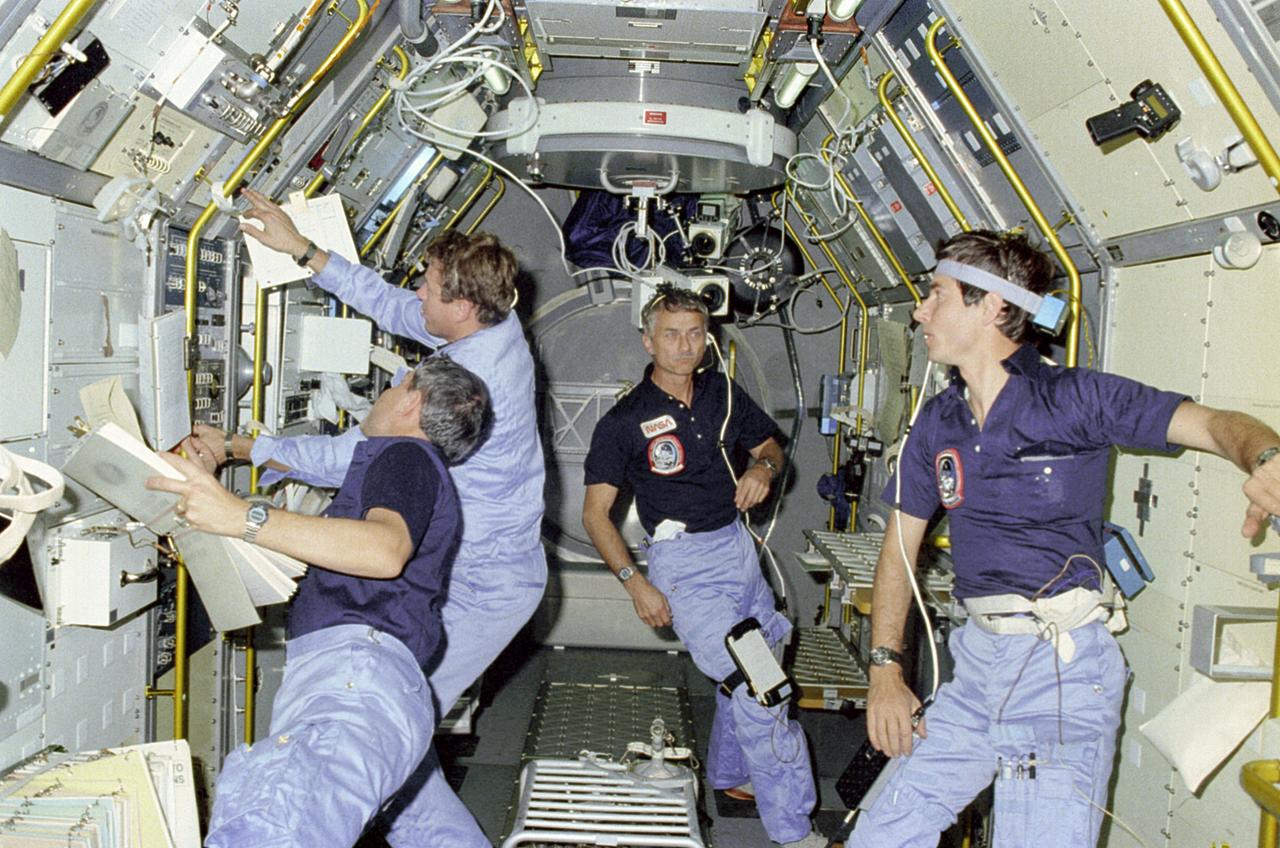 This photograph shows activities inside the science module during the Spacelab-1 (STS-9) mission. Left to right are Mission Specialist Robert Parker, Payload Specialist Byron Lichtenberg, Mission Specialist Owen Garriott, and Payload Specialist Ulf Merbold. The overall goal of the Spacelab-1 mission, the first mission of the Spacelab facility, were: (1) To verify the Spacelab system capability, (2) to obtain valuable scientific, applications, and technology data from a U.S./European multidisciplinary payload, and (3) to demonstrate the broad capability of Spacelab for scientific research. More than 70 experiments in 5 disciplines from 14 nations were conducted during the mission. The mission marked the the entry of non-astronaut persornel, called Payload Specialists, into space as working members of the crew. They are fellow scientists representing the international group of investigators using the mission. Mission Specialists are NASA astronauts who have broad scientific training. They operate various Orbiter-Spacelab systems, perform any required activity outside the spacecraft, and support investigations as needed. The Space Shuttle Orbiter Columbia that carried Spacelab-1 was operated by two other NASA astronauts serving as commander and pilot. The STS-9 mission, managed by the Marshall Space Flight Center, was launched on November 28, 1983.