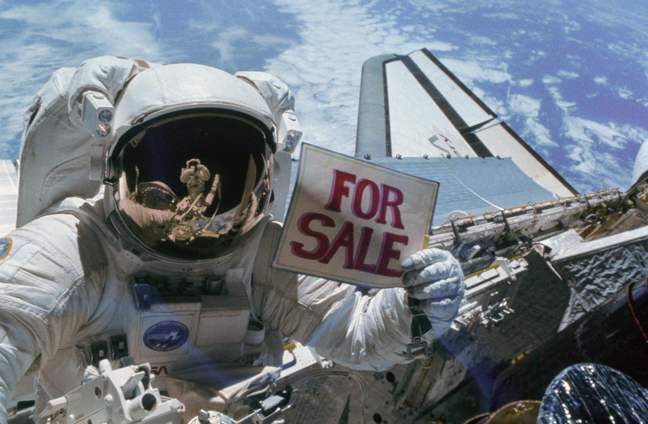 Astronauts are clowning around in space in this STS-51A onboard photo. Astronaut Gardner, holds a “For Sale” sign after the retrieval of two malfunctioning satellites; the Western Union Telegraph Communication Satellite (WESTAR VI); and the PALAPA-B2 Satellite. Astronaut Allen, who is standing on the Remote Manipulator System (RMS) is reflected in Gardner’s helmet visor. The 51A mission launched aboard the Space Shuttle Discovery on November 8, 1984.