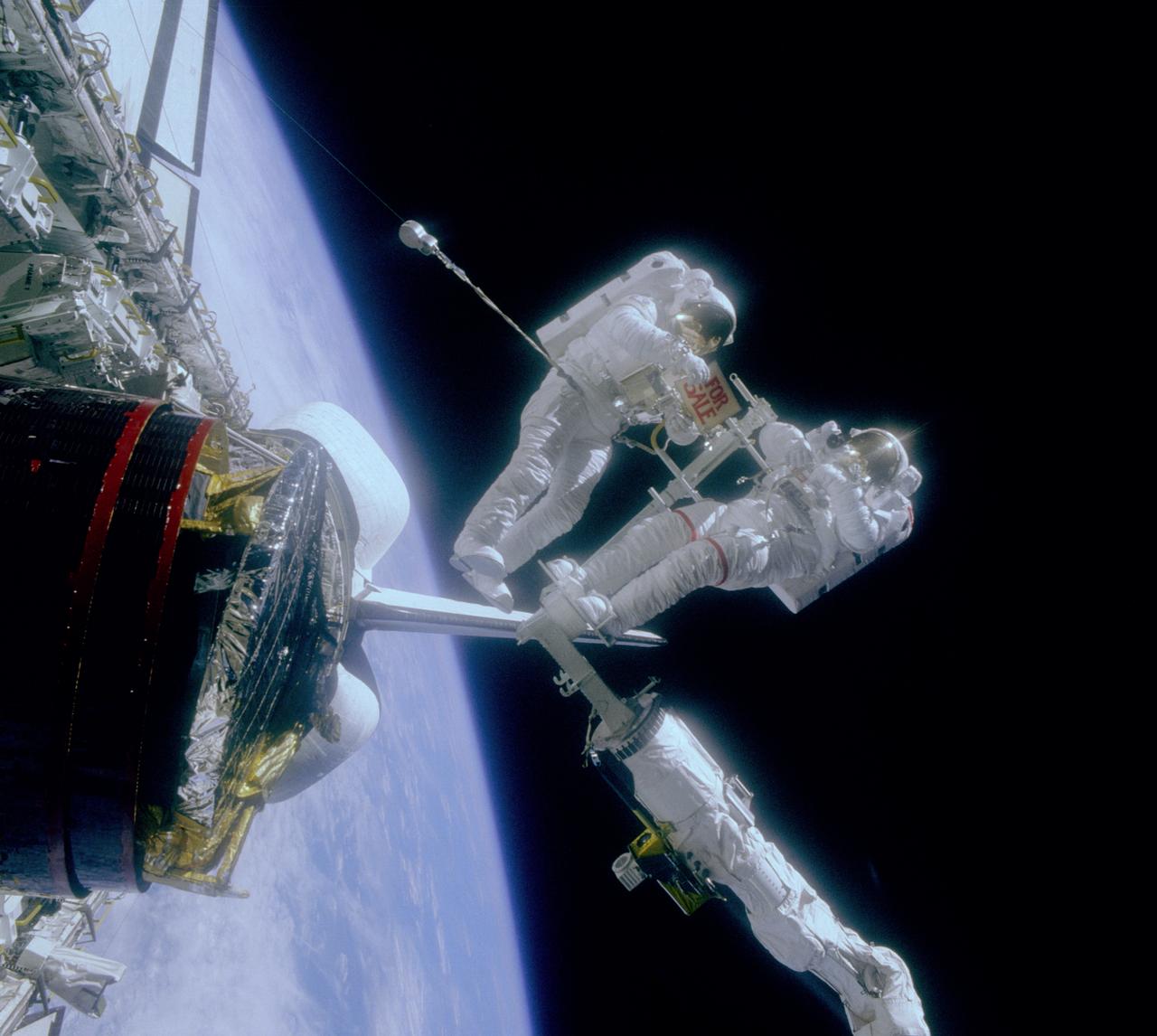 Astronauts are clowning around in space in this STS-51A onboard photo. Astronaut Gardner, holds a “For Sale” sign after the retrieval of two malfunctioning satellites; the Western Union Telegraph Communication Satellite (WESTAR VI); and the PALAPA-B2 Satellite. Astronaut  Allen, who is standing on the RMS (Remote Manipulator System) is reflected in Gardner’s helmet visor. The 51A mission launched aboard the Space Shuttle Discovery on November 8, 1984.