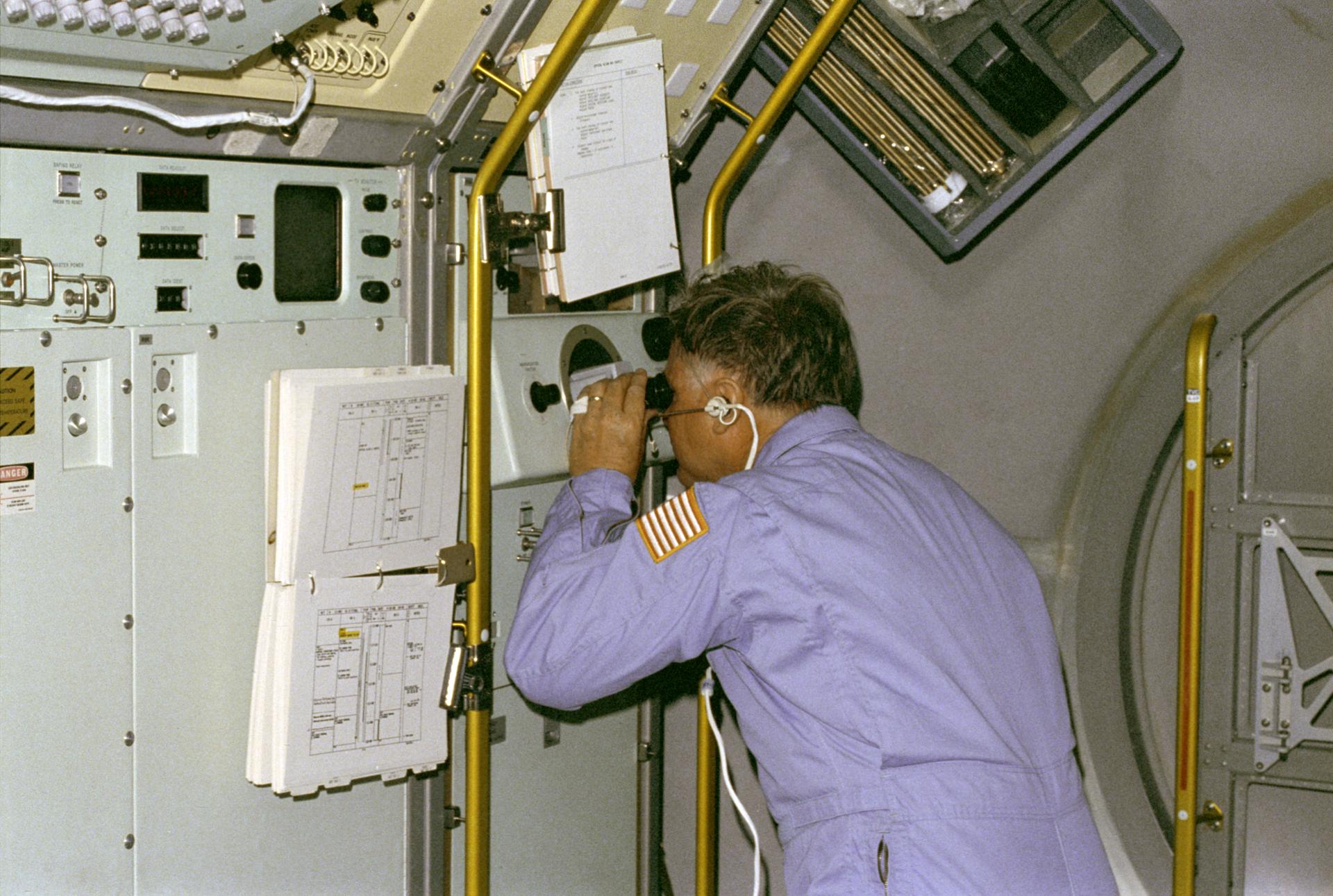 Astronaut Don Lind looks through a microscope at the vapor crystal growth furnace on Spacelab 3
