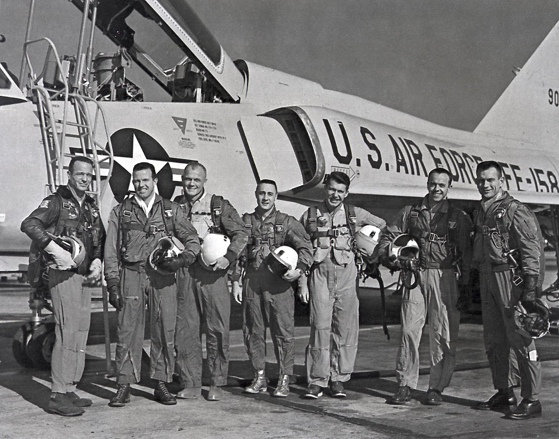 The original seven astronauts for the Mercury Project pose in front of an Air Force Jet.