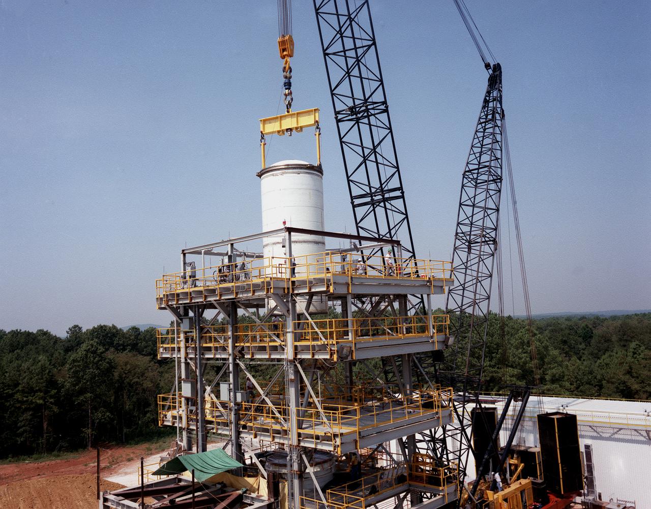 A forward segment is being lowered into the Transient Pressure Test Article (TPTA) test stand at the Marshall Space Flight Center (MSFC) east test area. The TPTA test stand, 14-feet wide, 27-feet long, and 33-feet high, was built in 1987 to provide data to verify the sealing capability of the redesign solid rocket motor (SRM) field and nozzle joints. The test facility applies pressure, temperature, and external loads to a short stack of solid rocket motor hardware. The simulated SRM ignition pressure and temperature transients are achieved by firing a small amount of specially configured solid propellant. The pressure transient is synchronized with external programmable dynamic loads that simulate lift off loads at the external tank attach points. Approximately one million pounds of dead weight on top of the test article simulates the weight of the other Shuttle elements.