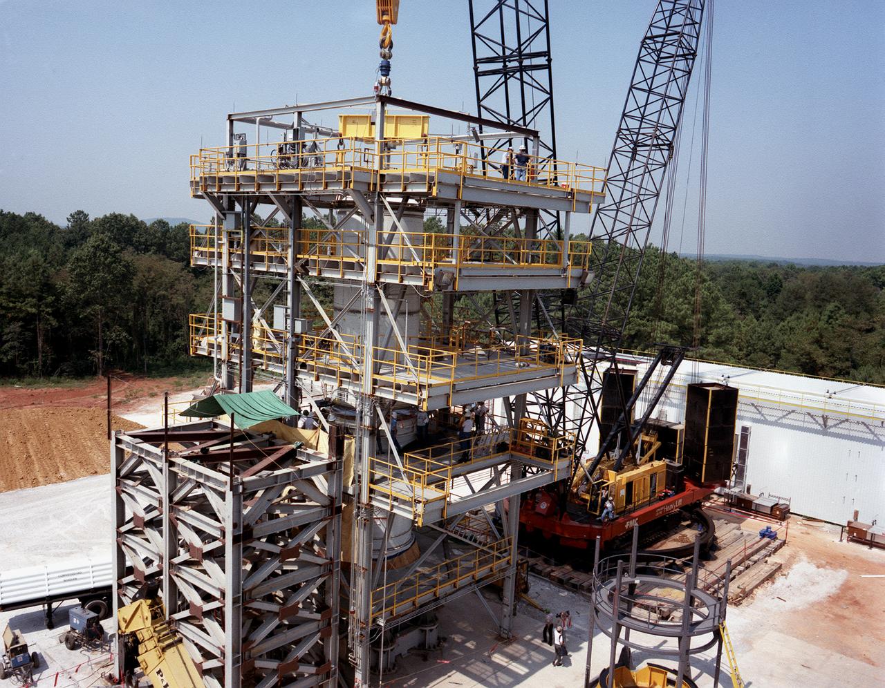 A forward segment is being lowered into the Transient Pressure Test Article (TPTA) test stand at thw Marshall Space Flight Center (MSFC) east test area. The TPTA test stand, 14-feet wide, 27-feet long, and 33-feet high, was built in 1987 to provide data to verify the sealing capability of the redesign solid rocket motor (SRM) field and nozzle joints. The test facility applies pressure, temperature, and external loads to a short stack of solid rocket motor hardware. The simulated SRM ignition pressure and temperature transients are achieved by firing a small amount of specially configured solid propellant. The pressure transient is synchronized with external programmable dynamic loads that simulate lift off loads at the external tank attach points. Approximately one million pounds of dead weight on top of the test article simulates the weight of the other Shuttle elements.