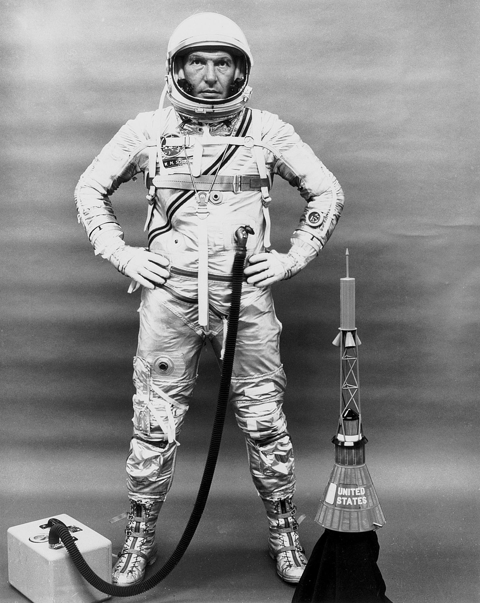 Wally Schirra stands with his hands on his hips wearing his Mercury space suit