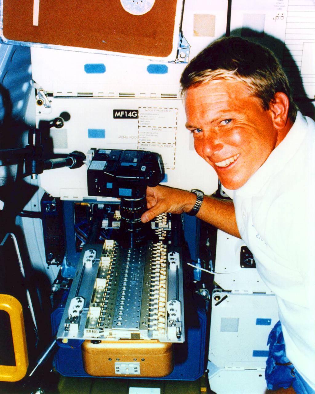 Mission Specialist George (Pinky) D. Nelson uses a 35 mm camera to photograph a protein crystal grown during the STS-26 Protein Crystal Growth (PCG-II-01) experiment. The protein crystal growth (PCG) carrier is shown deployed from the PCG Refrigerator/Incubator Mocule (R/IM) located in the middeck forward locker. The R/IM contained three Vapor Diffusion Apparatus (VDS) trays (one of which is shown). A total of sixty protein crystal samples were processed during the STS-26 mission.