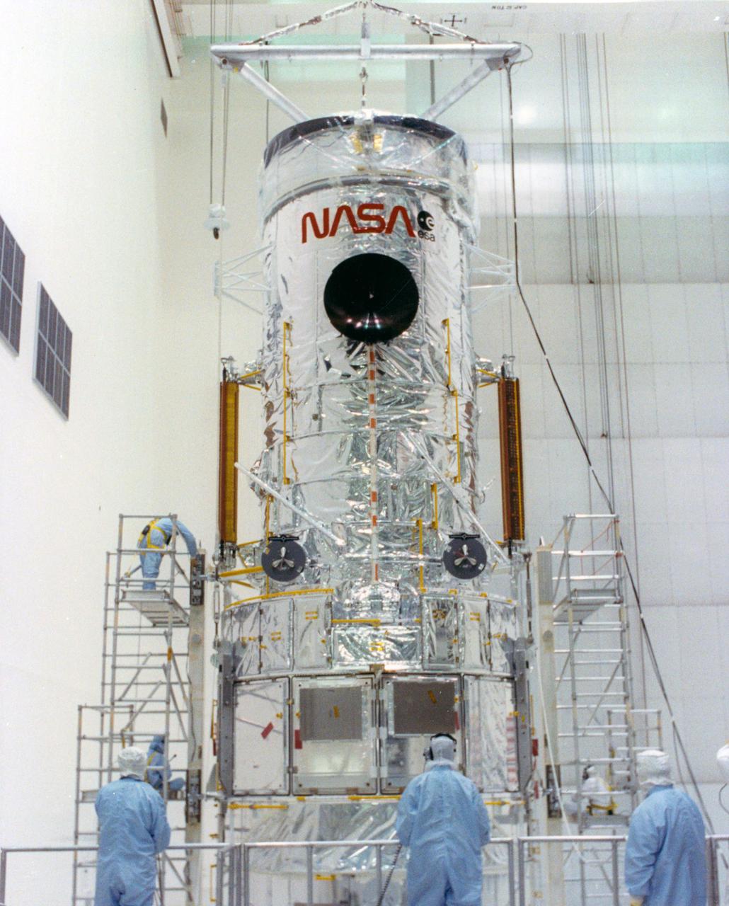 KENNEDY SPACE CENTER, FLA. -- The Hubble Space Telescope (HST) is lifted into the workstands in the Vertical Processing Facility as work begins at KSC to process the 94-inch primary mirror telescope for launch on Discovery on Space Shuttle Mission STS-31 in March 1990. With HST, astronomers will be able to view 97 percent of the known universe, and will be able to get pictures unlimited and undistorted by the Earth's atmosphere. Compared with earth-based observatories, the HST will be able to view celestial objects that are 50 times fainter, provide images that are 10 times sharper, and see objects that are seven times farther away. .