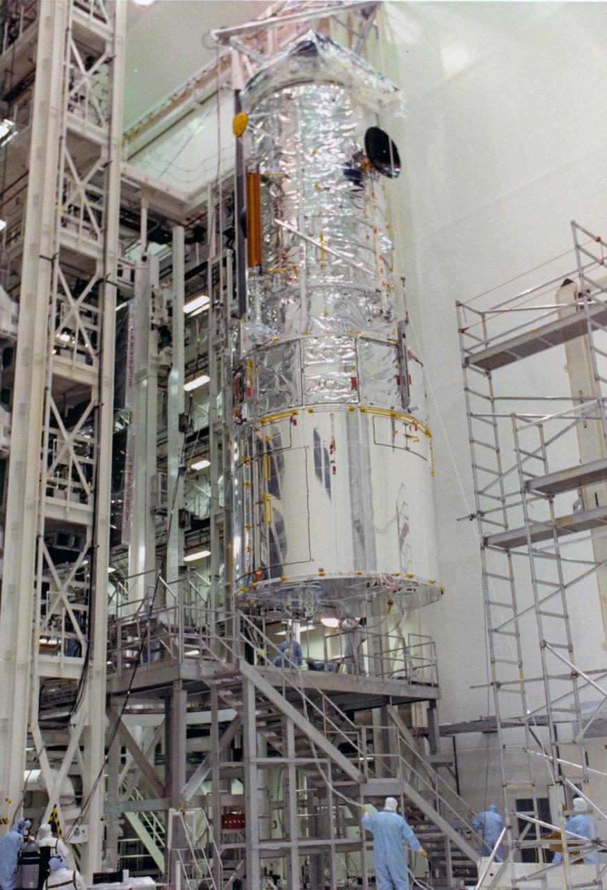 KENNEDY SPACE CENTER, FLA. -- The Hubble Space Telescope (HST) is lifted into the workstands in the Vertical Processing Facility as work begins at KSC to process the 94-inch primary mirror telescope for launch on Discovery on Space Shuttle Mission STS-31 in March 1990. With HST, astronomers will be able to view 97 percent of the known universe, and will be able to get pictures unlimited and undistorted by the Earth's atmosphere. Compared with earth-based observatories, the HST will be able to view celestial objects that are 50 times fainter, provide images that are 10 times sharper, and see objects that are seven times farther away. .